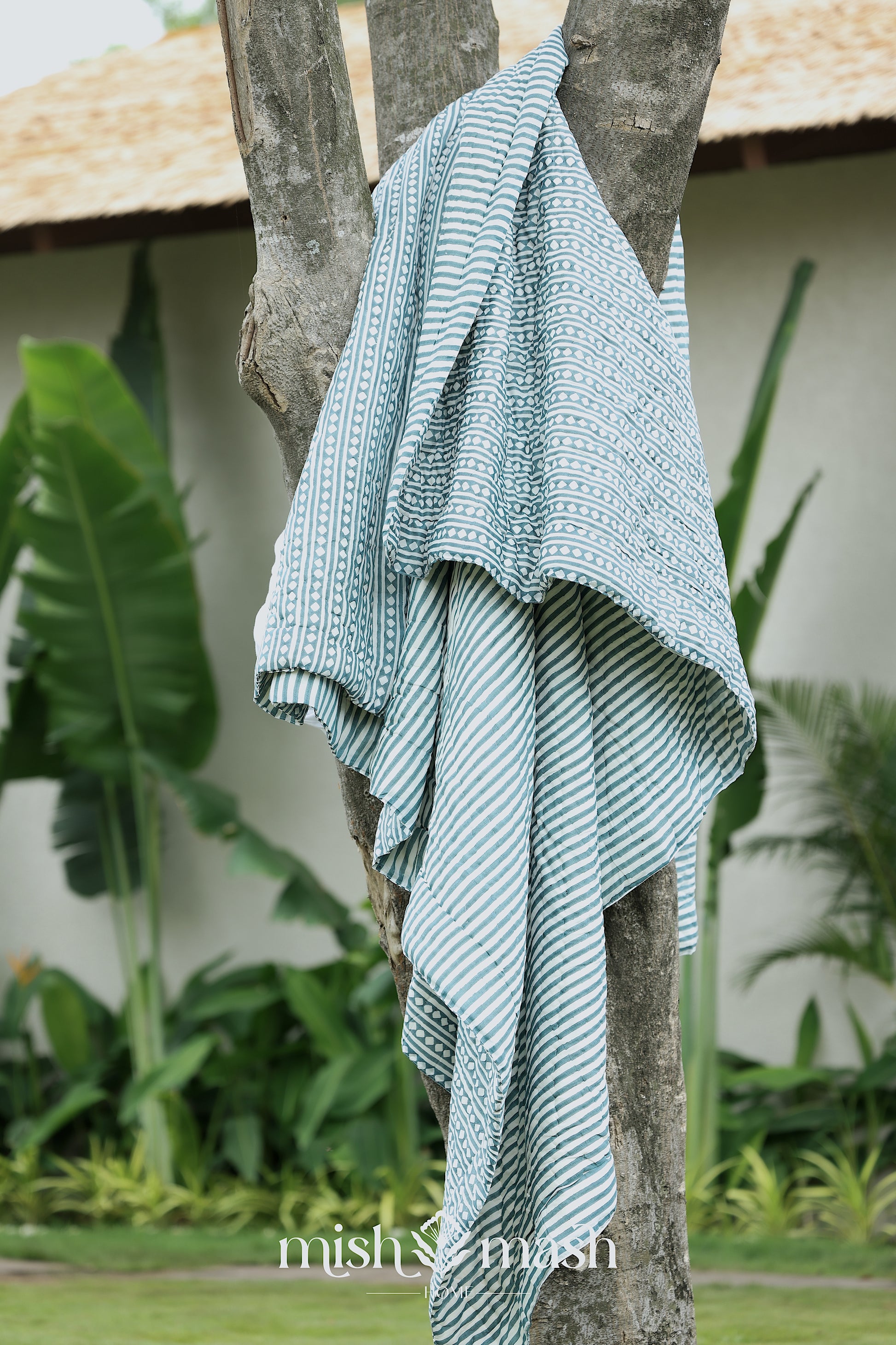 blue stripped jaipuri quilt draped over a tree branch with 'mish mish' branding in the corner.