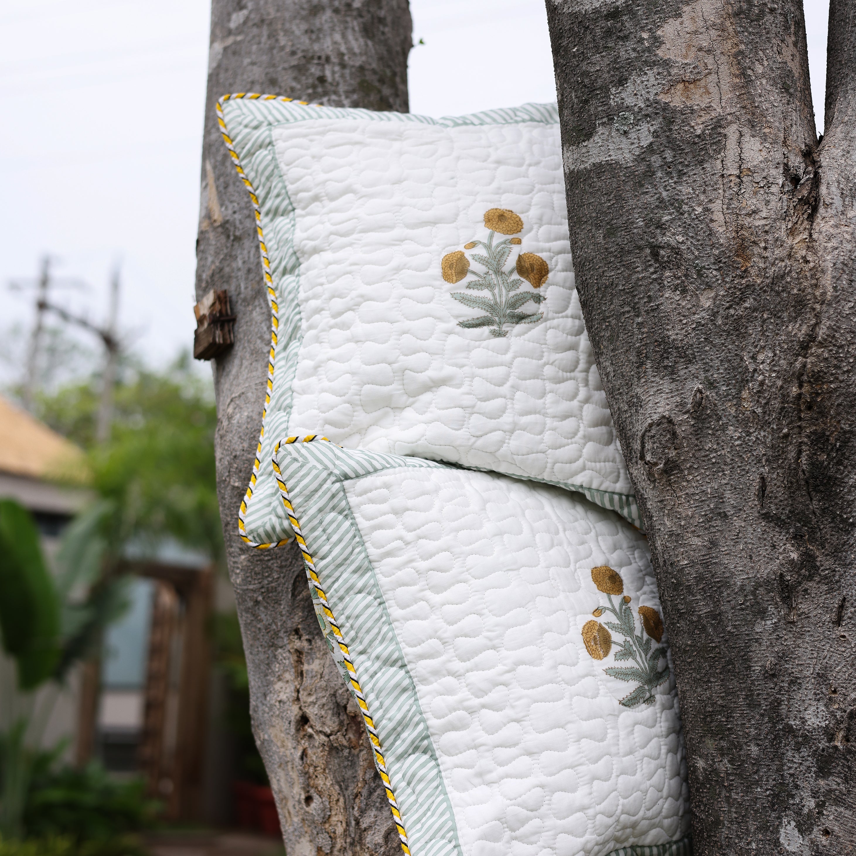 Quilted yellow Cushion cover with floral print hanging on a tree. Buy cushion covers online.
