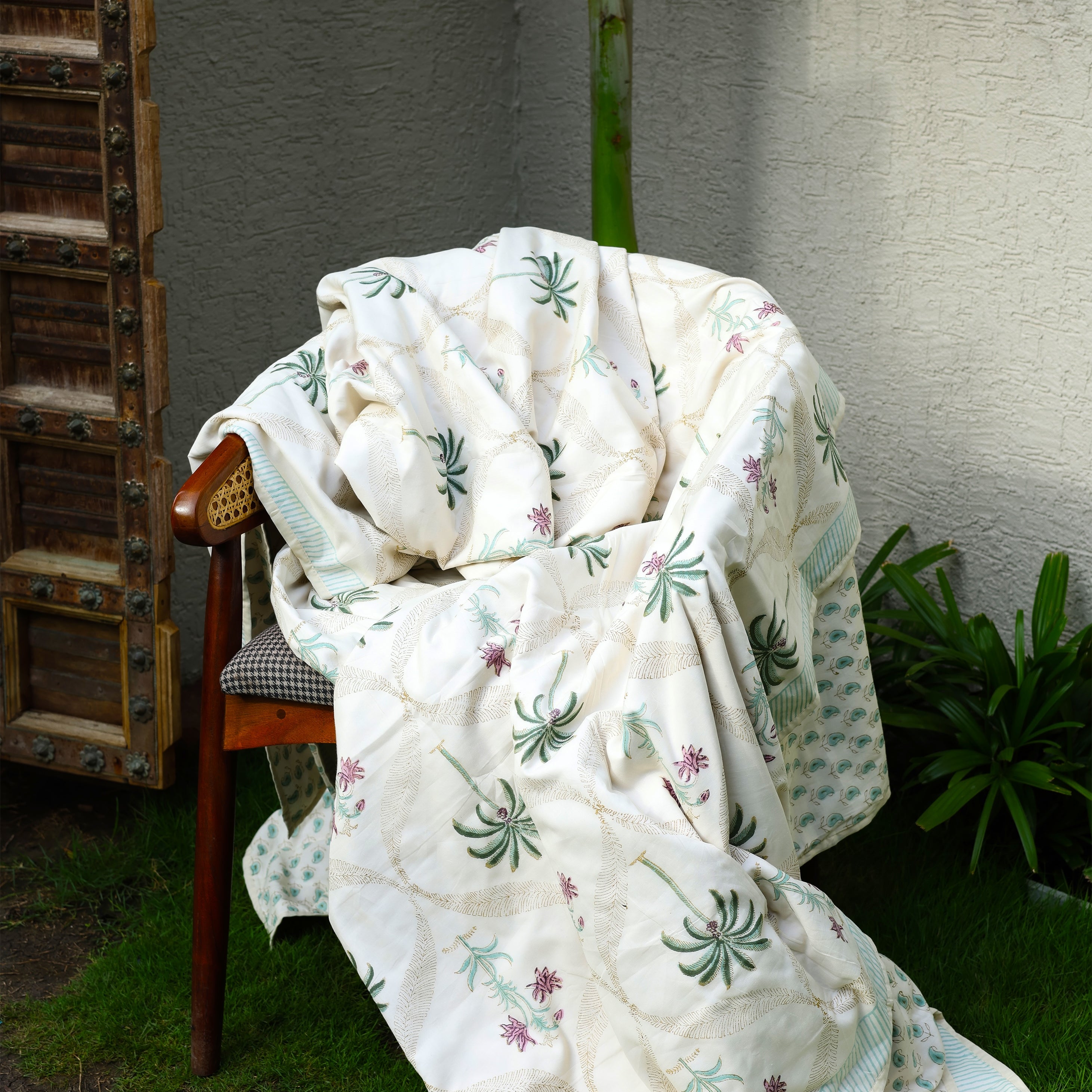 White floral cotton dohar blanket draped over a chair with palm motifs handprinted
