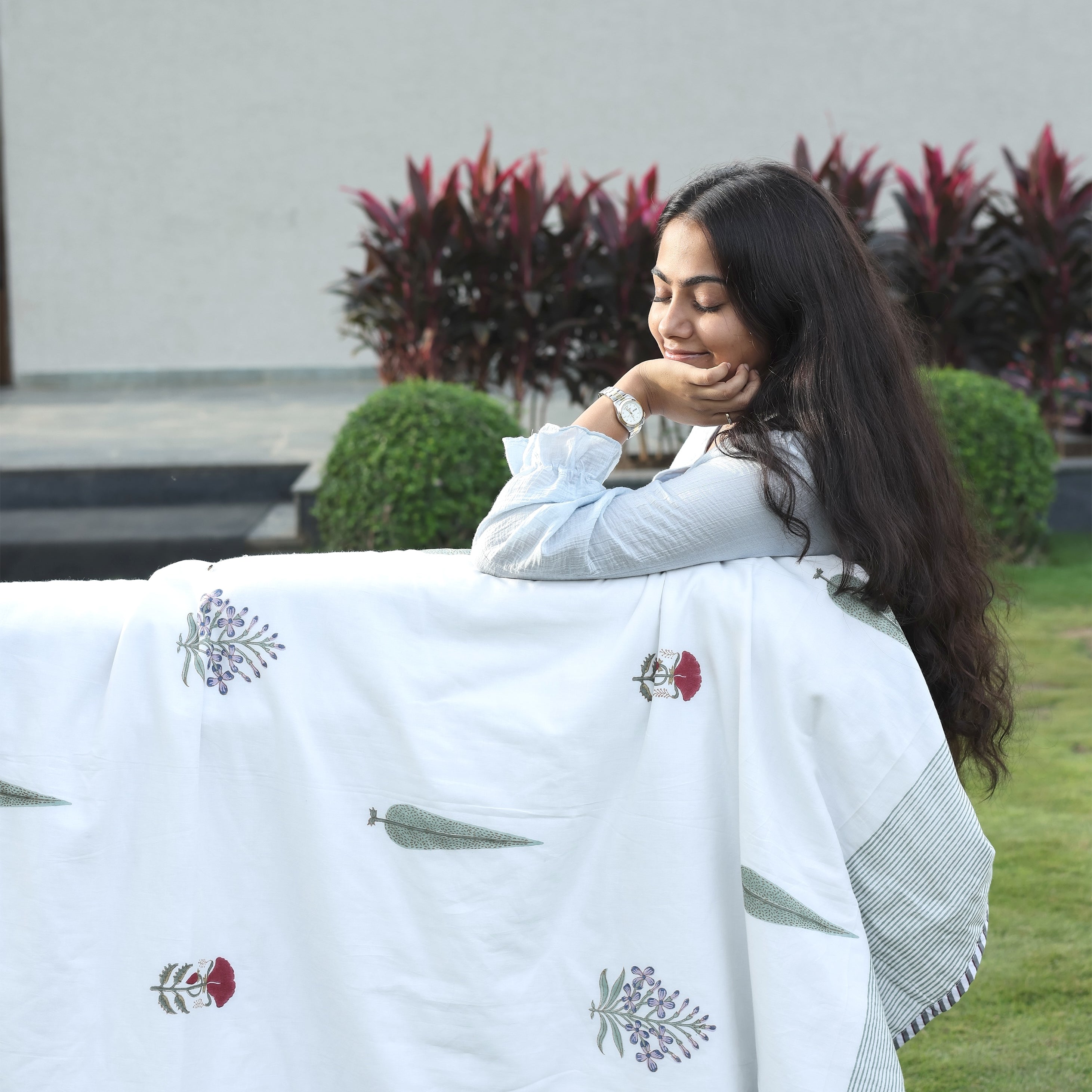 Woman wrapped in a white floral cotton dohar blanket with 'mish mash' branding in an outdoor setting. Cotton dohar.
