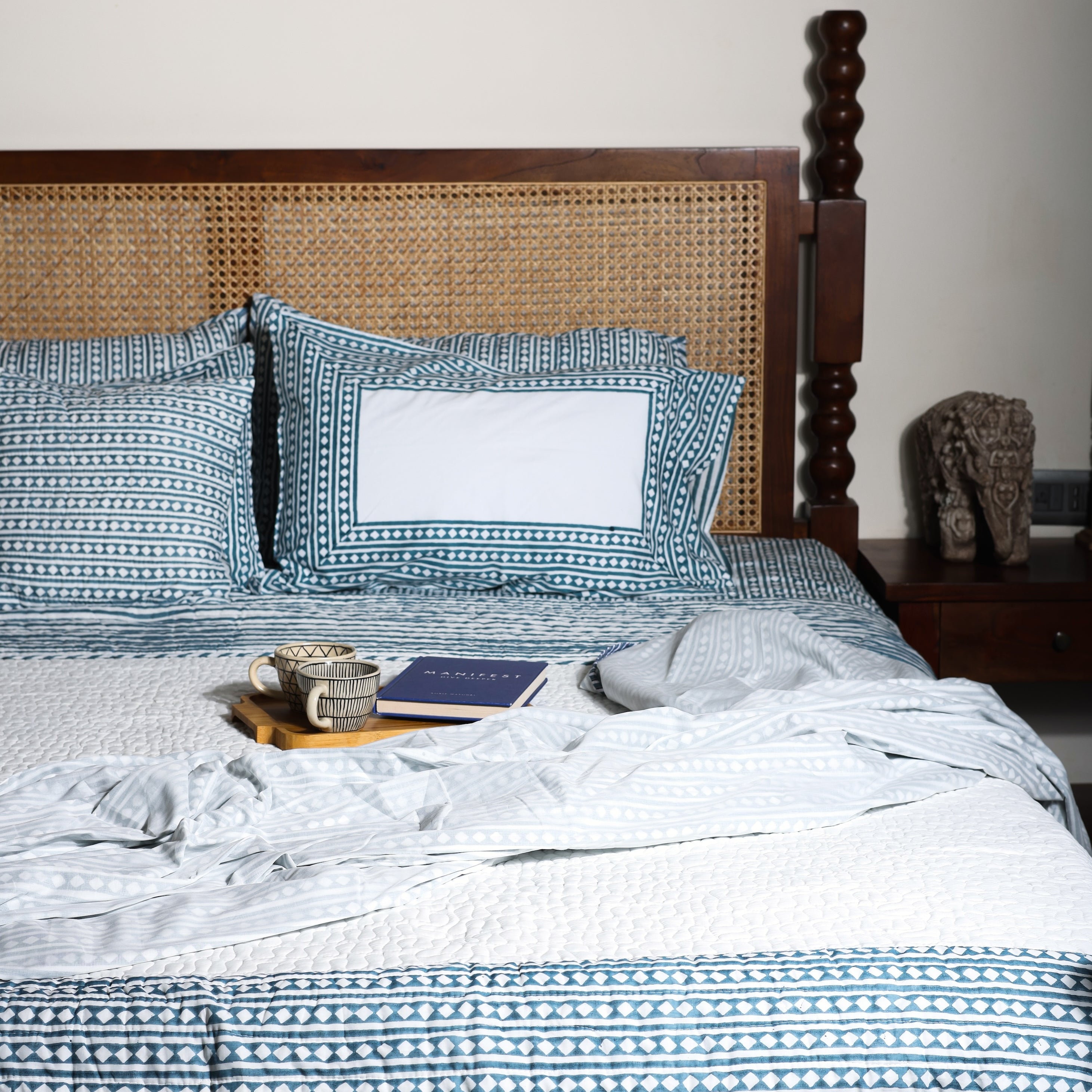 Bed with blue and white geometric double bed bedsheet and a cotton bedspread and cotton dohar blanket on top.