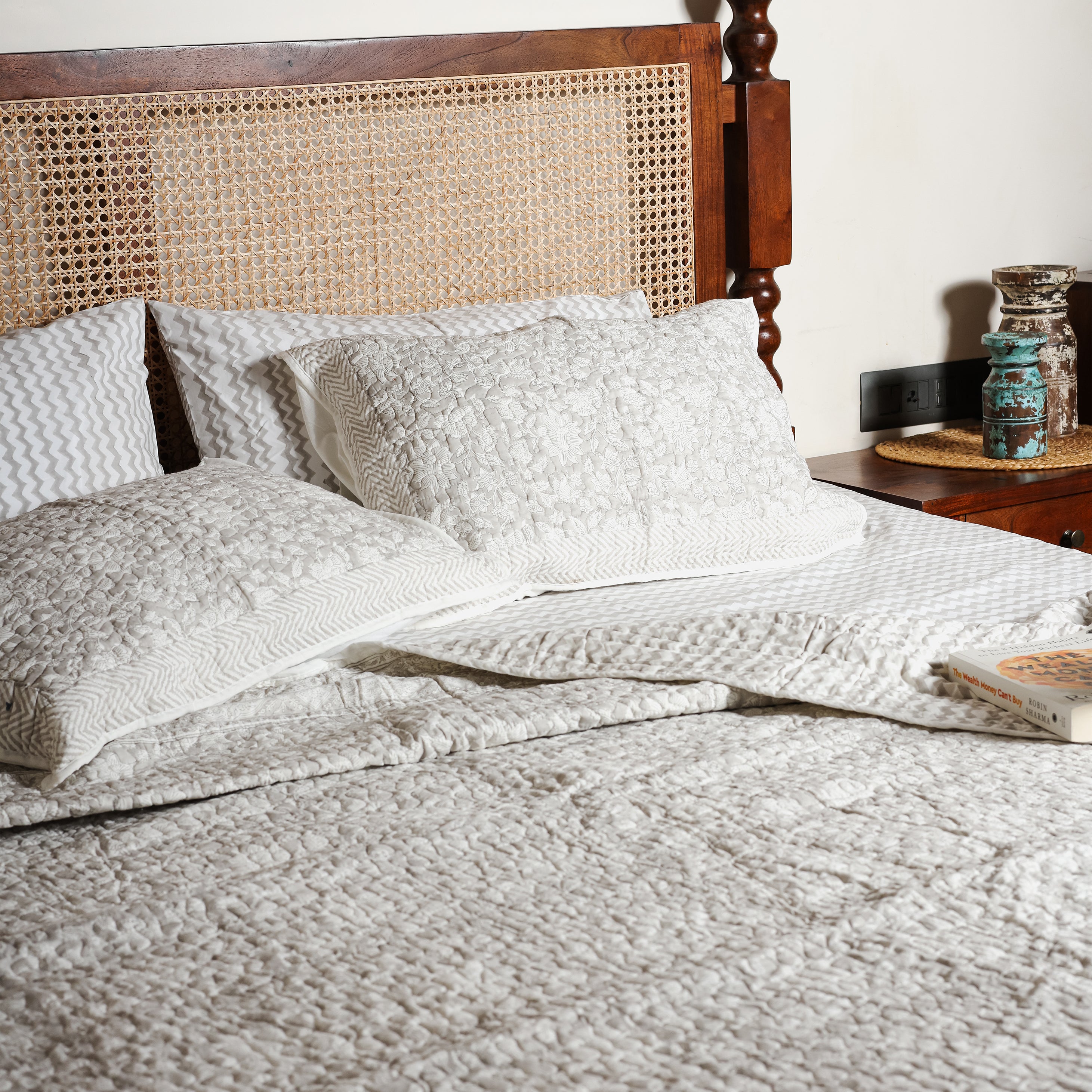 Bed with grey reversible bed spread and pillows, featuring floral design on side and chevron design on another in pure cotton