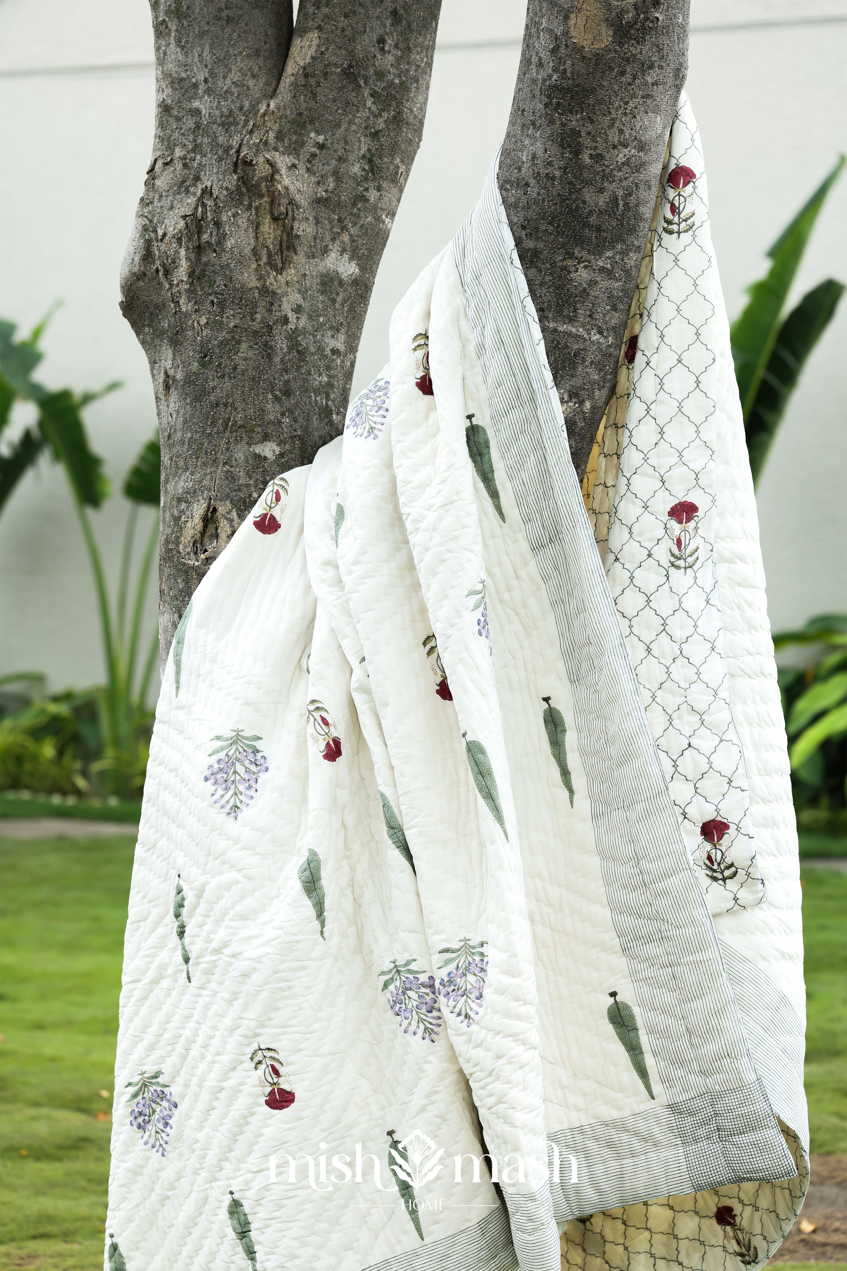 White quilt with floral block print draped over a tree branch outdoors. Buy cotton razai. Buy jaipur rajai.