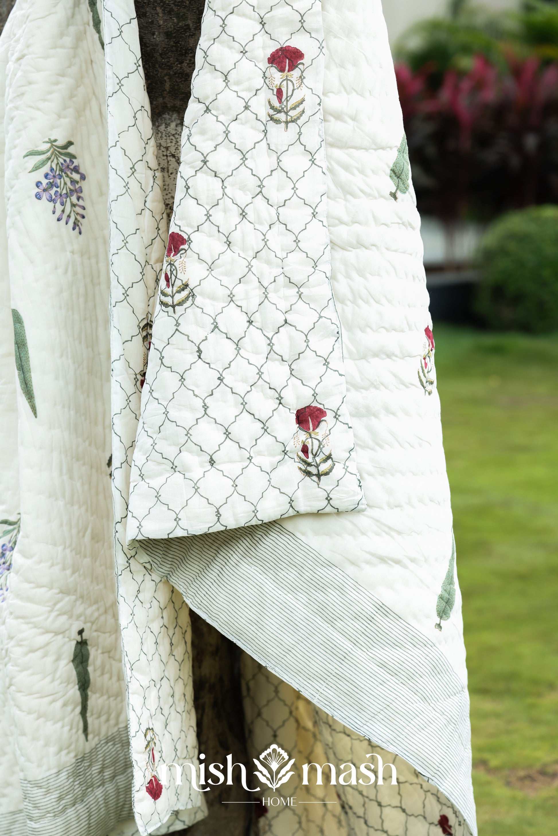 White quilt with floral blockprint on a wooden tree outdoors. Jaipuri razai.