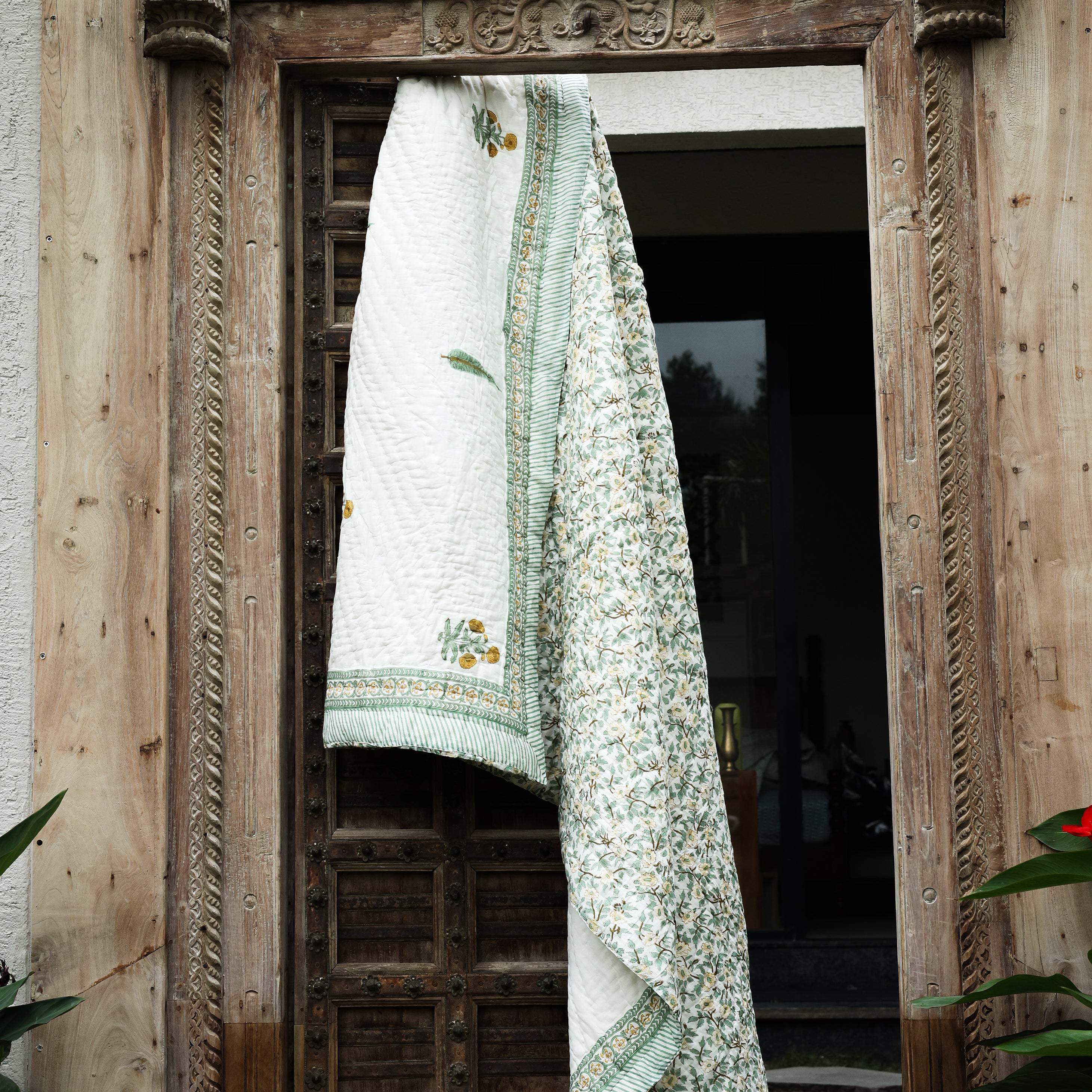 Decorative jaipuri quilt with yellow and green patterns hanging on a wooden door. Buy jaipuri quilts online.