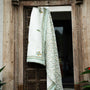 Decorative jaipuri quilt with yellow and green patterns hanging on a wooden door. Buy jaipuri quilts online.