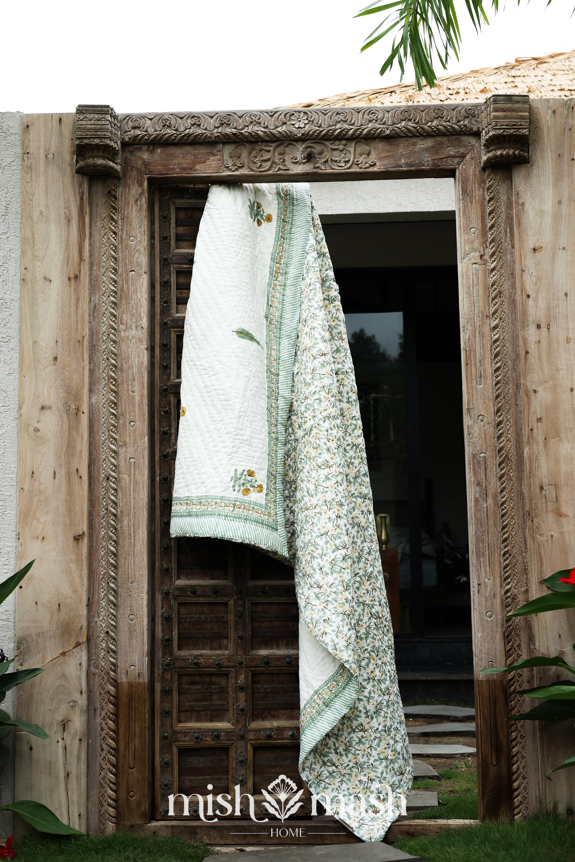 Decorative jaipuri quilt with yellow and green patterns hanging on a wooden door. Buy jaipuri quilts online.
