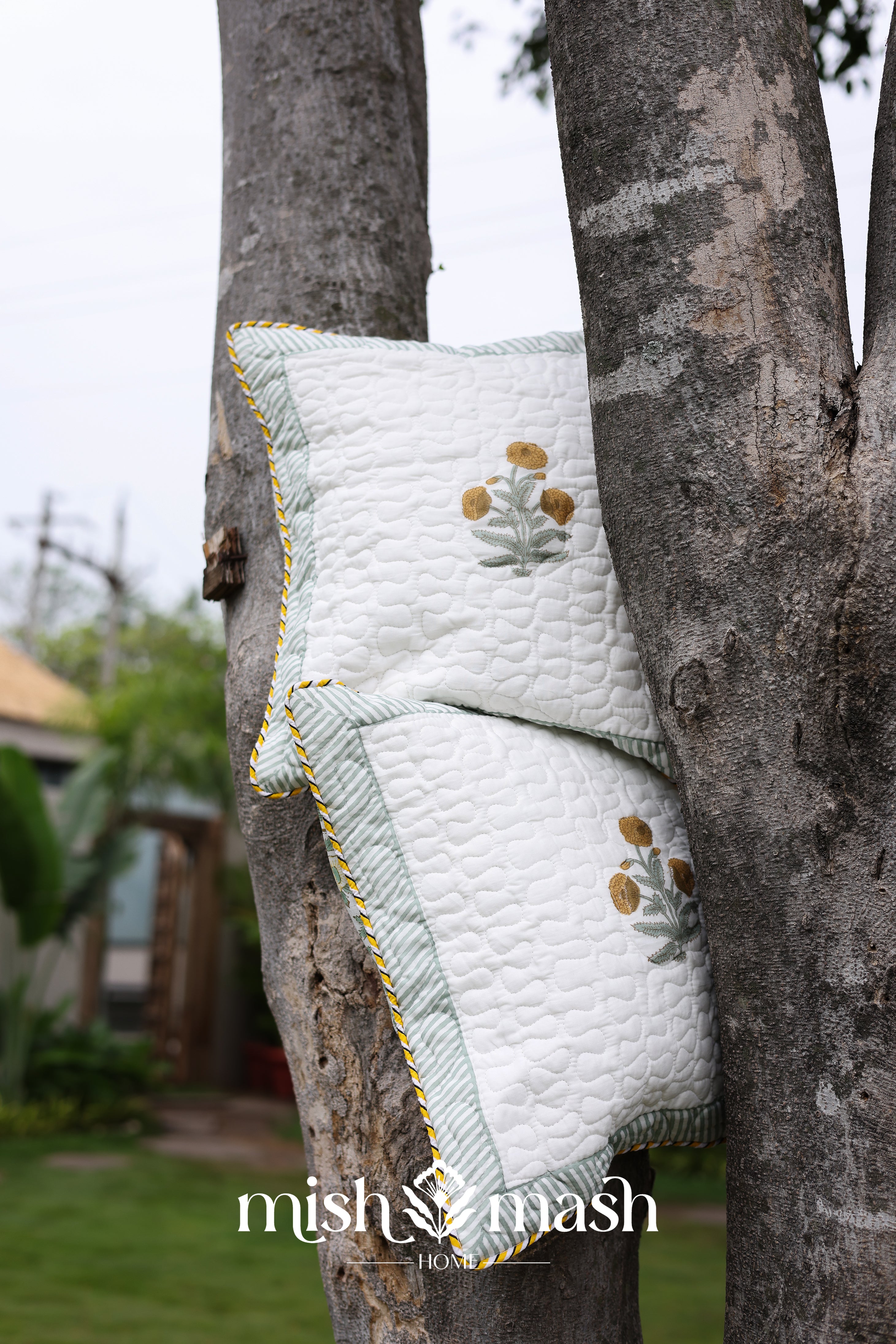 Quilted yellow Cushion cover with floral print hanging on a tree. Buy cushion covers online.