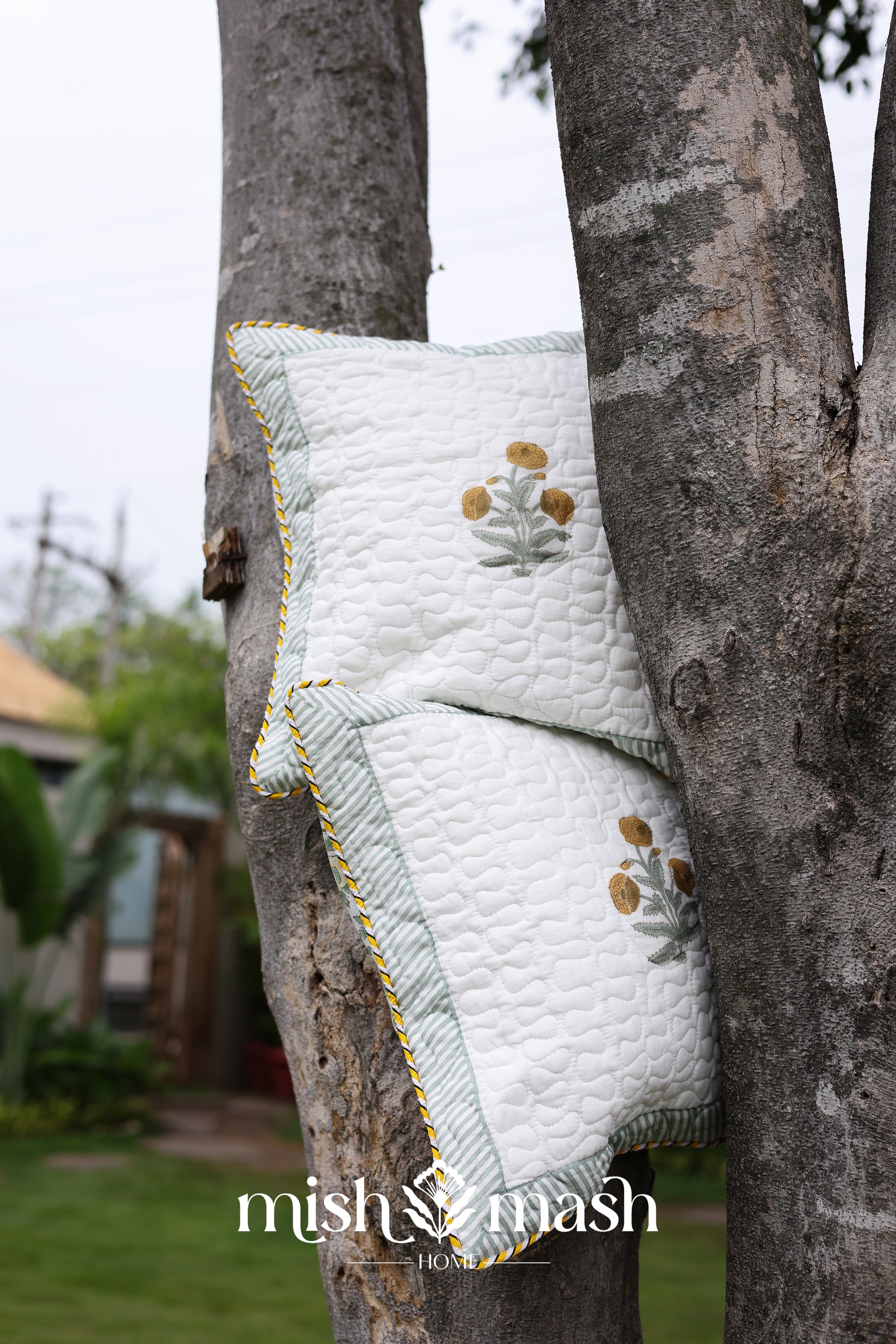 Quilted yellow Cushion cover with floral print hanging on a tree. Buy cushion covers online.