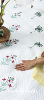 Person sitting on a floral-patterned quilted bed cover perfect as housewarming gift. Buy luxury bedspread online.