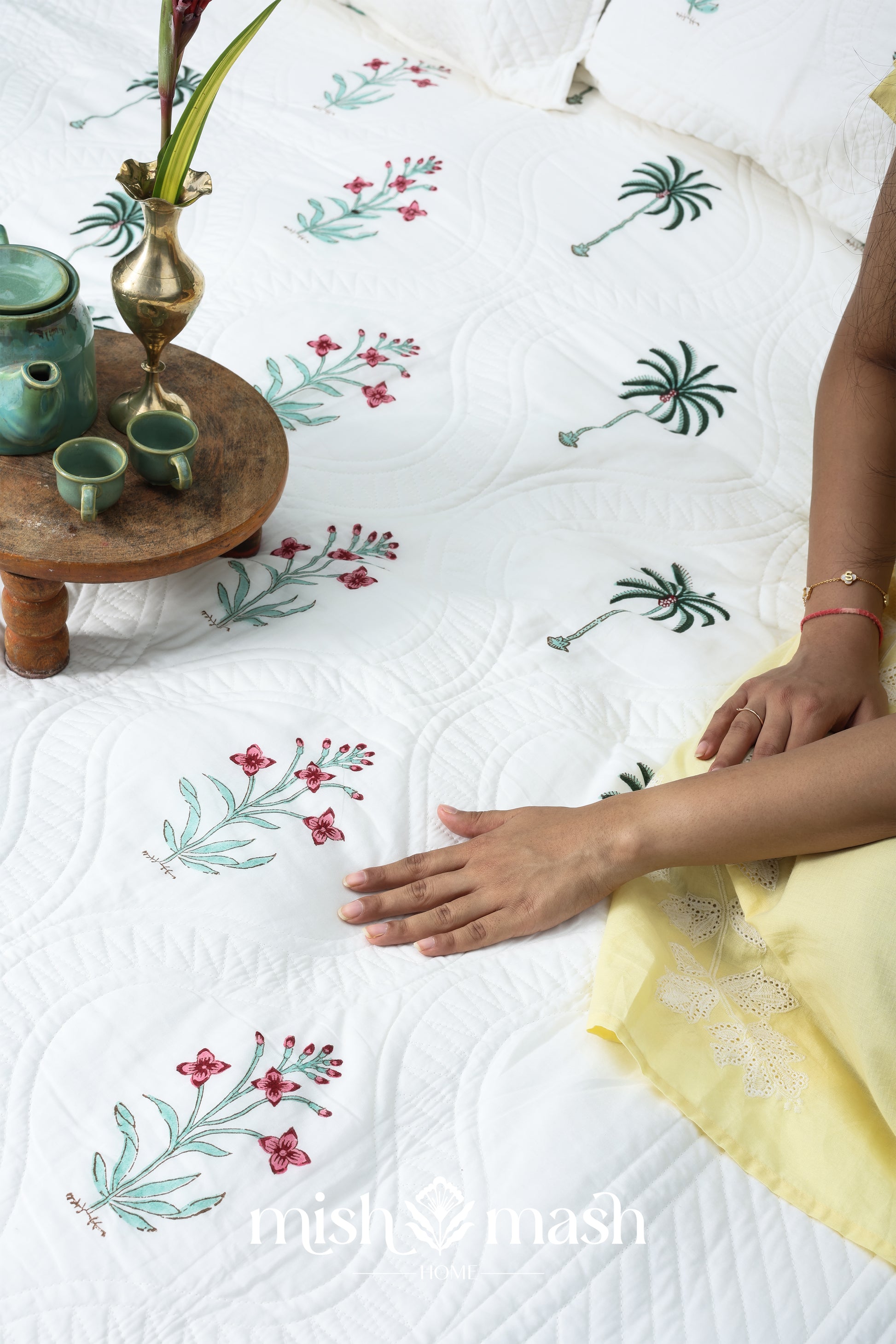 Person sitting on a floral-patterned quilted bed cover perfect as housewarming gift. Buy luxury bedspread online.