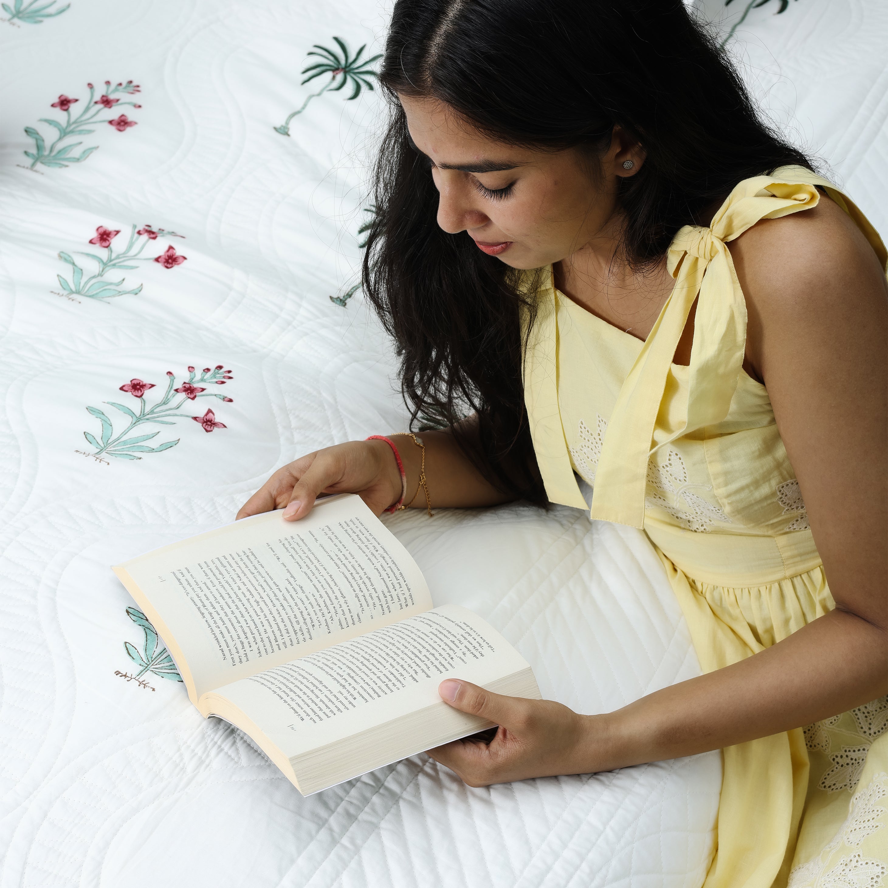 Woman reading a book on a bed with cotton bed cover perfect as a housewarming gift