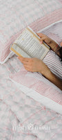 Woman reading a book on a bed with red and white reversible cotton bed spread, and two pillows with pure cotton pillow covers laying on the bed