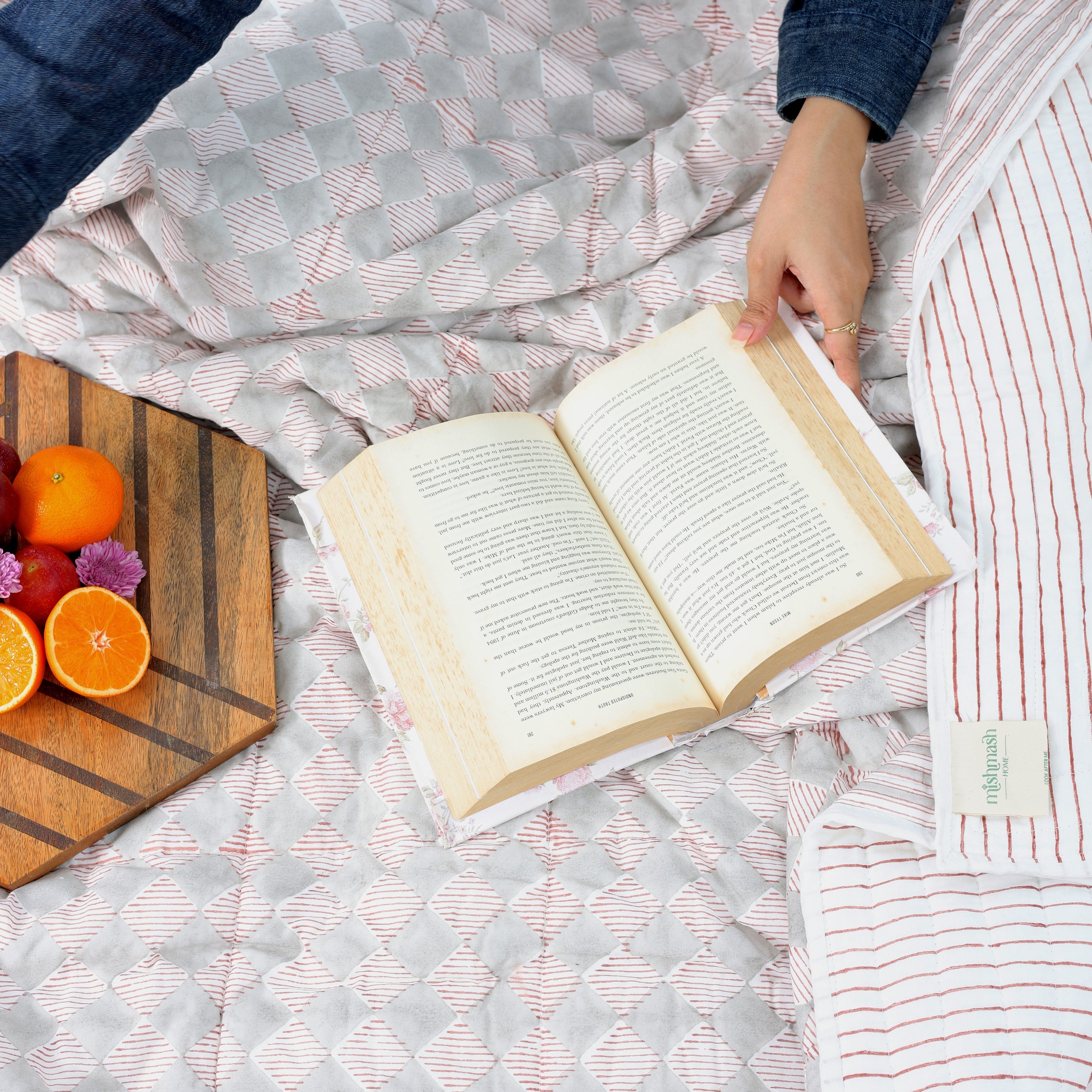 Person reading a book on a bed while using a cozy reversible red and white cotton dohar blanket