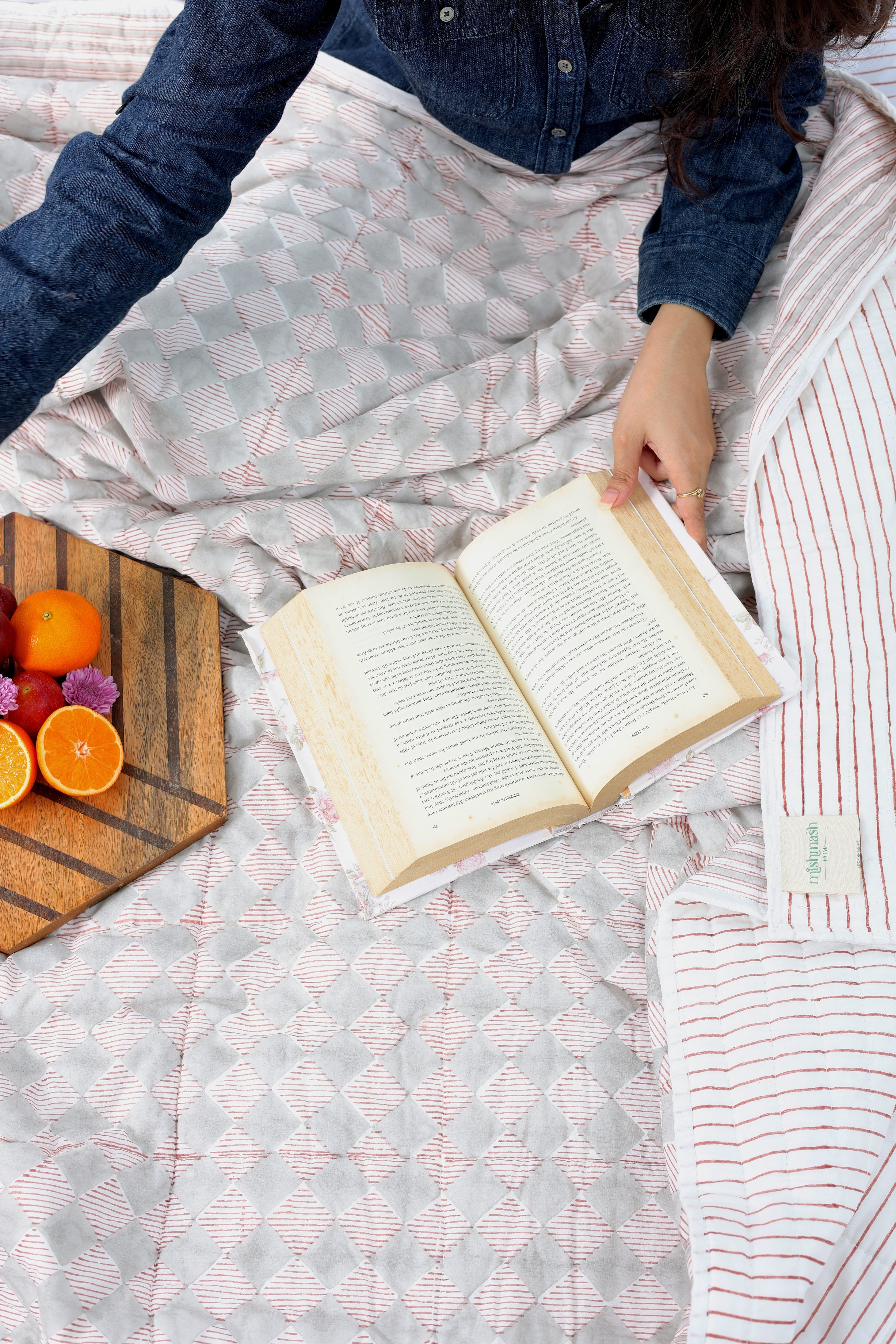 Person reading a book on a bed while using a cozy reversible red and white cotton dohar blanket