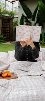 Person lying on a bed with a floral-patterned book while using a red and grey reversible Dohar blanket for summer