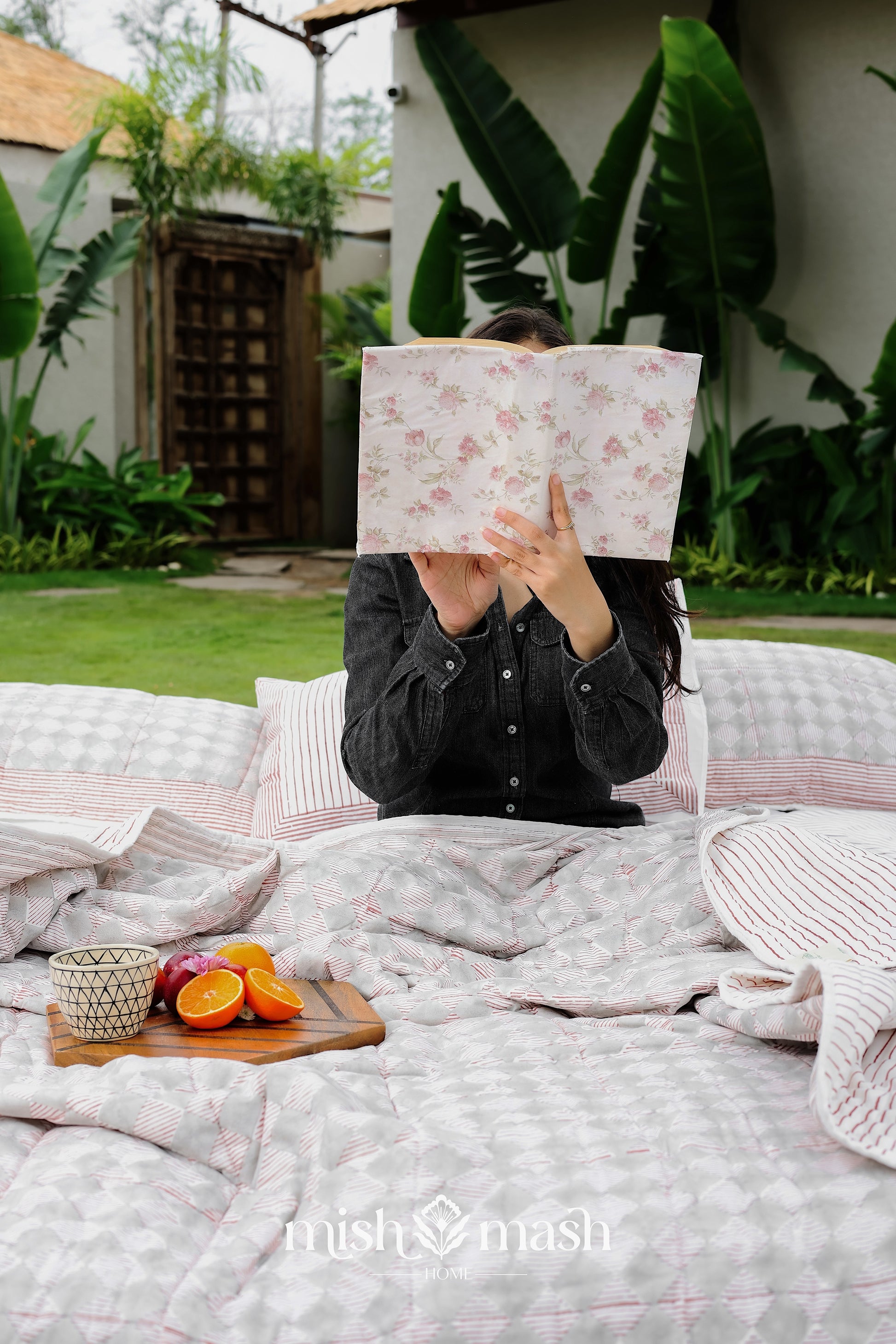 Person lying on a bed with a floral-patterned book while using a red and grey reversible Dohar blanket for summer