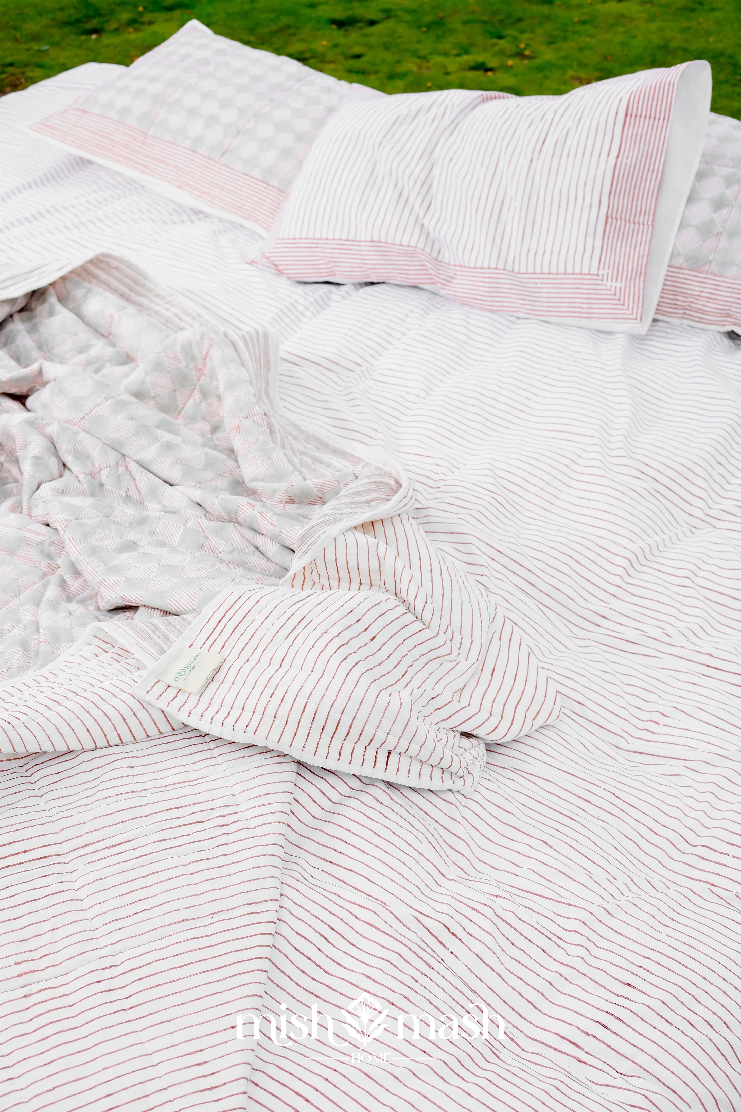red and white striped pure cotton double bed sheet laying on green grass with two pillows 