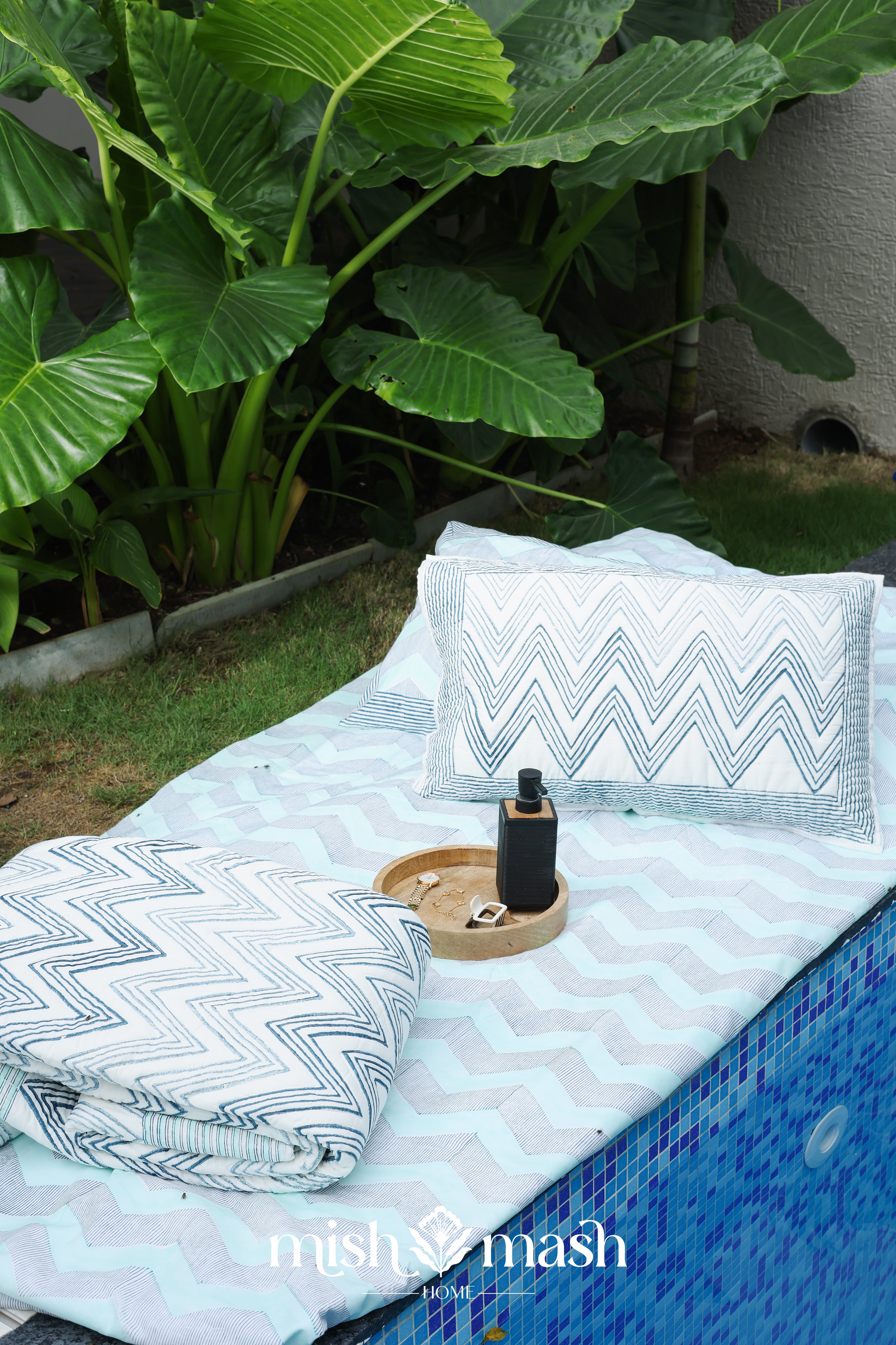 Outdoor setting with a blue chevron double bed sheet and folded reversible quilted bed spread along with two matching pillows
