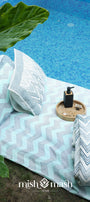 Blue cotton bed sheet with matching bedspread and two pillows laying near a pool