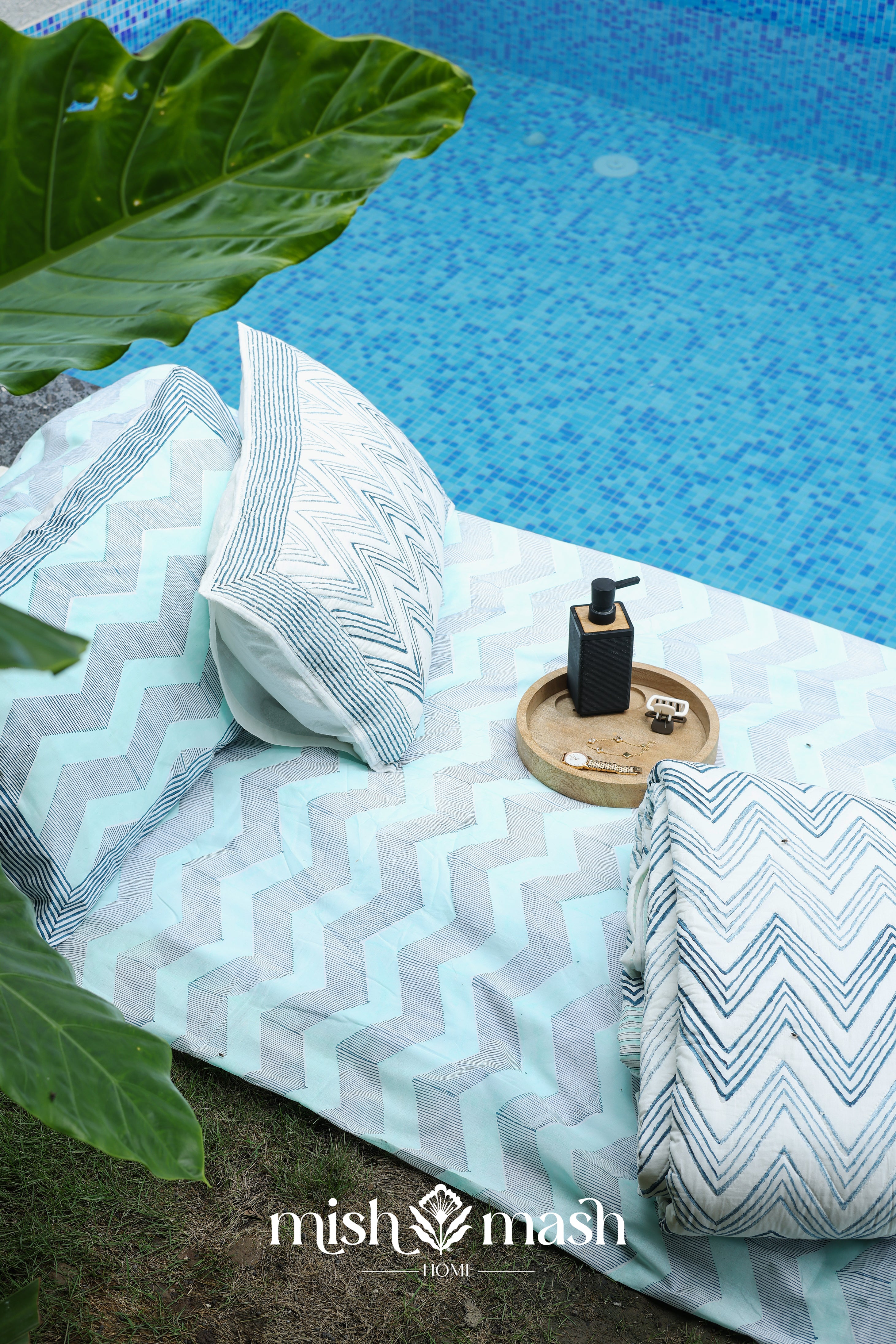 Blue cotton bed sheet with matching bedspread and two pillows laying near a pool