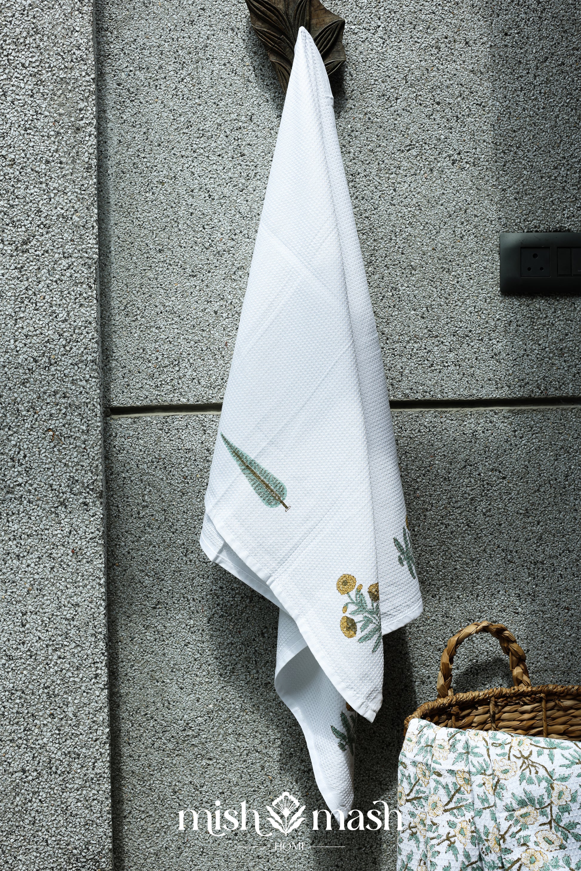 White towel hanging on a textured wall. Ladies bath towel with yellow floral print.