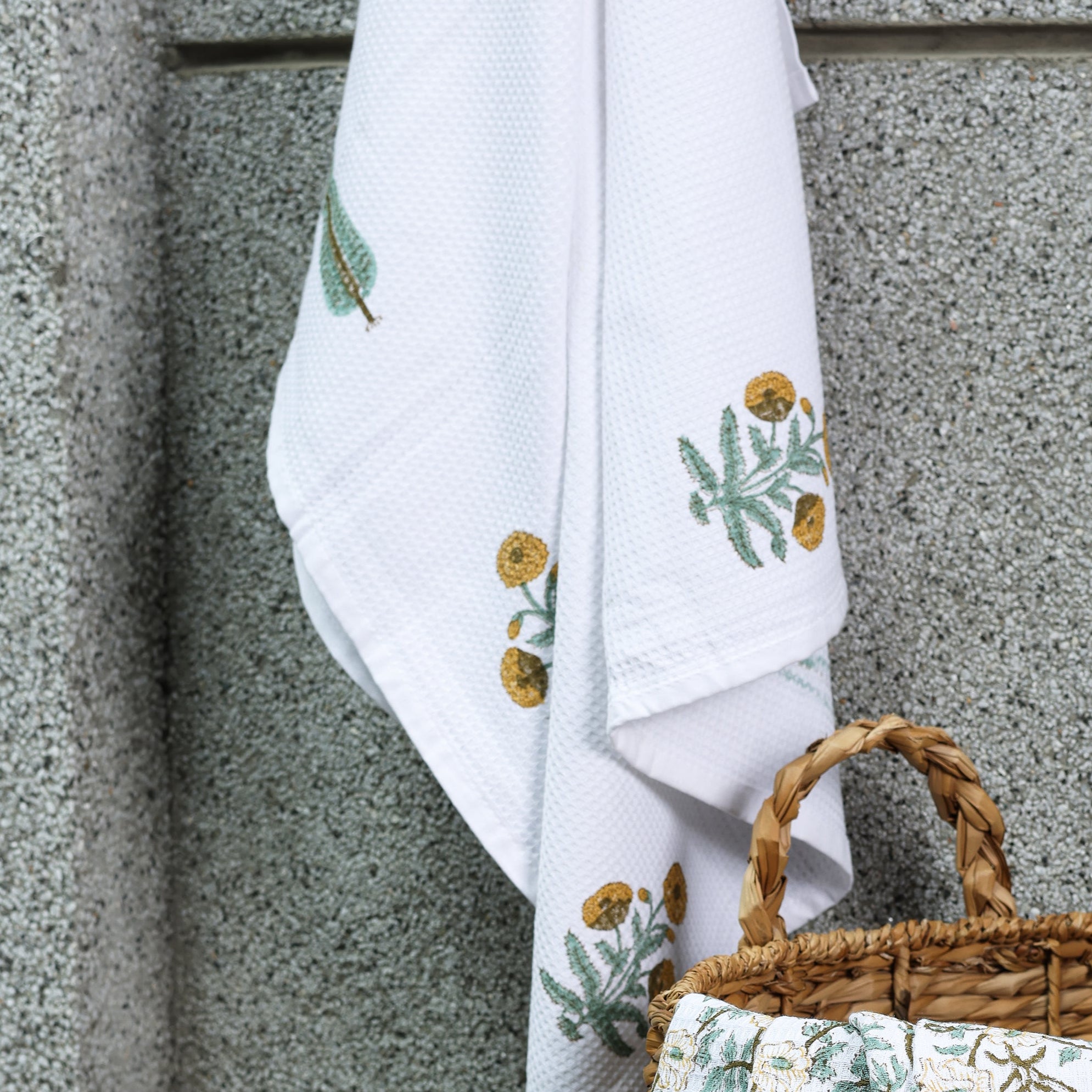 Woven basket and floral ladies bath towel against a textured wall. Buy bath linen online.