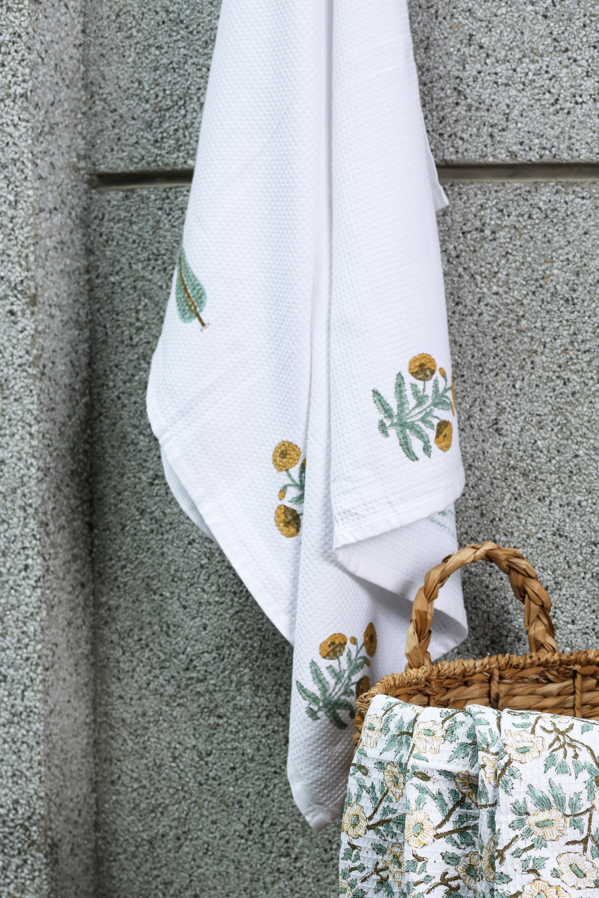 Woven basket and floral ladies bath towel against a textured wall. Buy bath linen online.