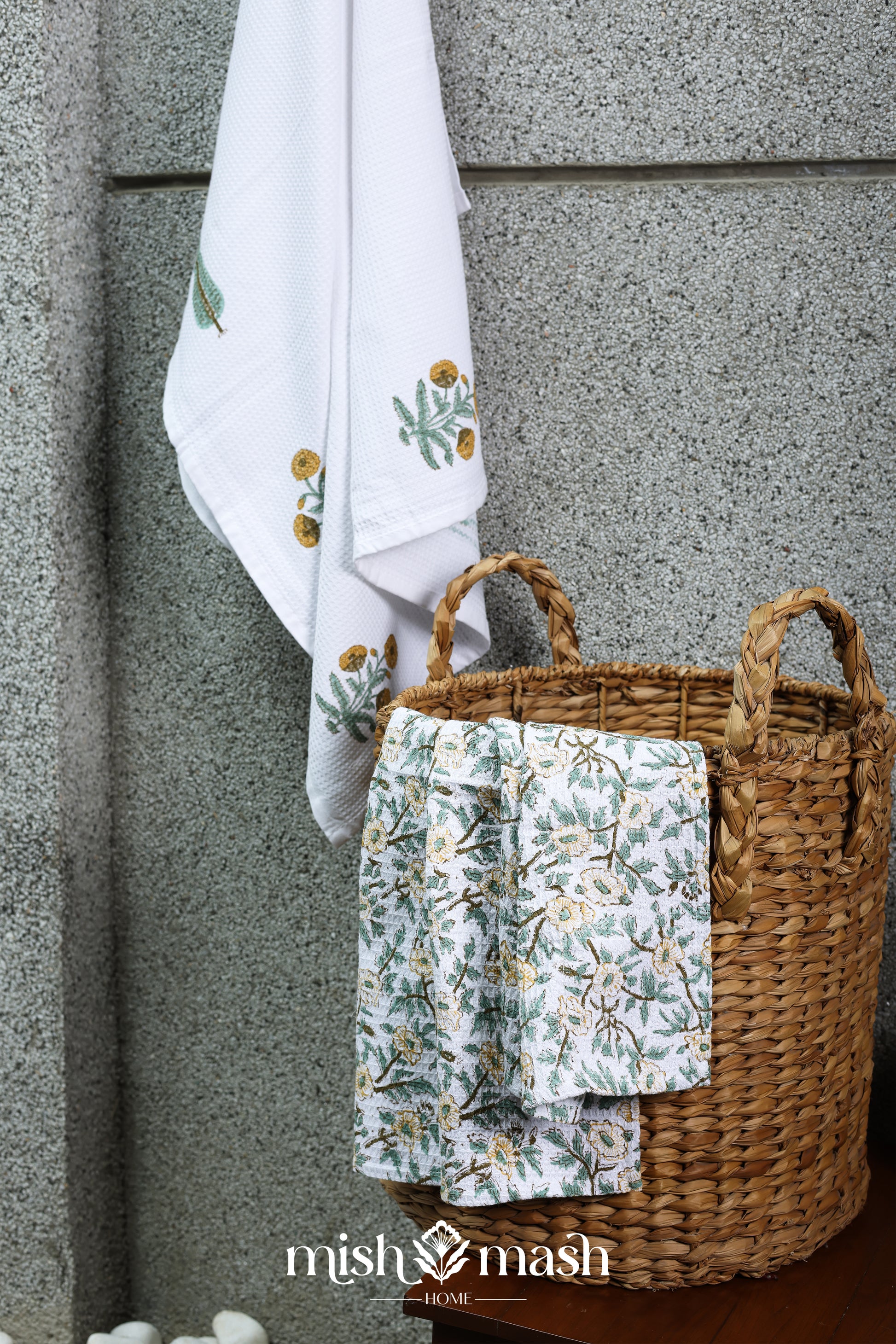 Woven basket having two hand towels and a quick dry bath towel against a textured wall.