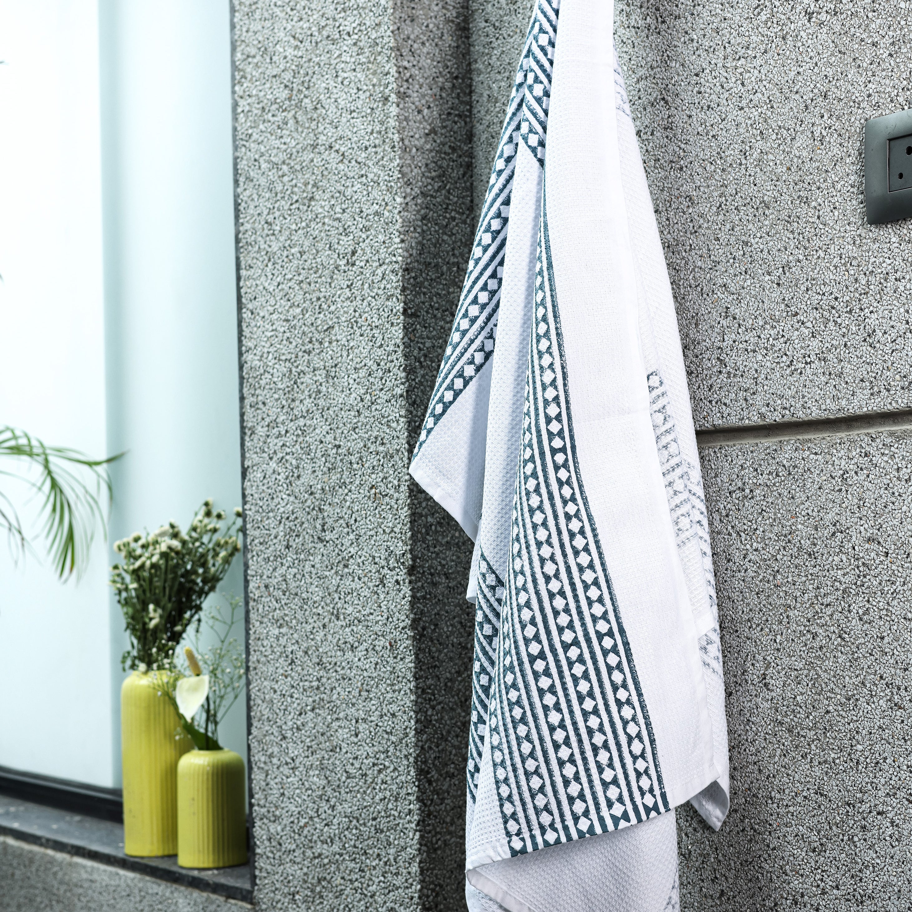 Cotton Bath Towel with a blue geometric pattern hanging on a wall. Trident bath towels.