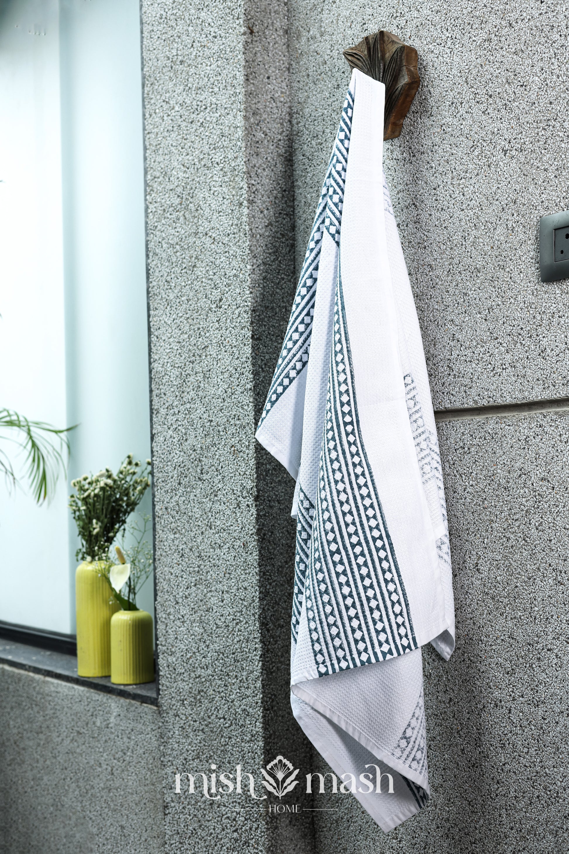 Cotton Bath Towel with a blue geometric pattern hanging on a wall. Trident bath towels.