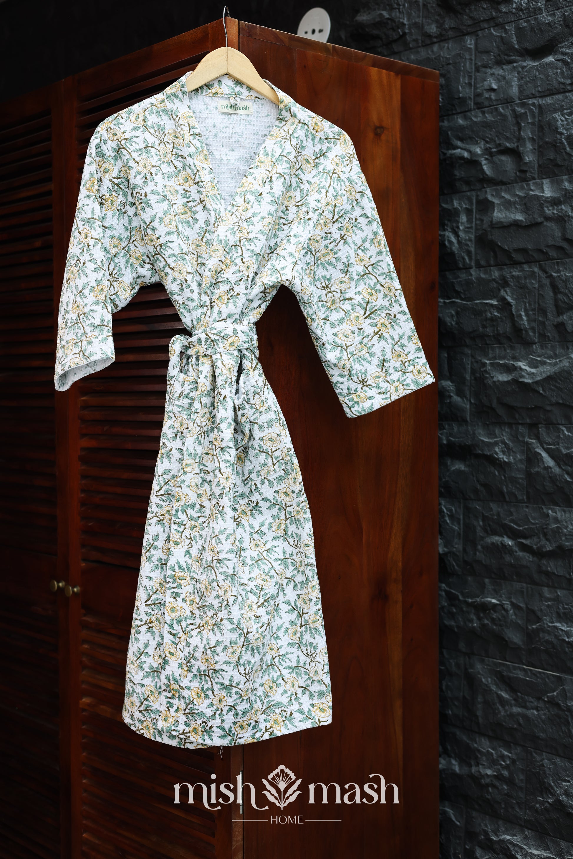 Floral-patterned cotton bath robe hanging on a wooden door with a stone wall background. Bombay dyeing bath robe for women.