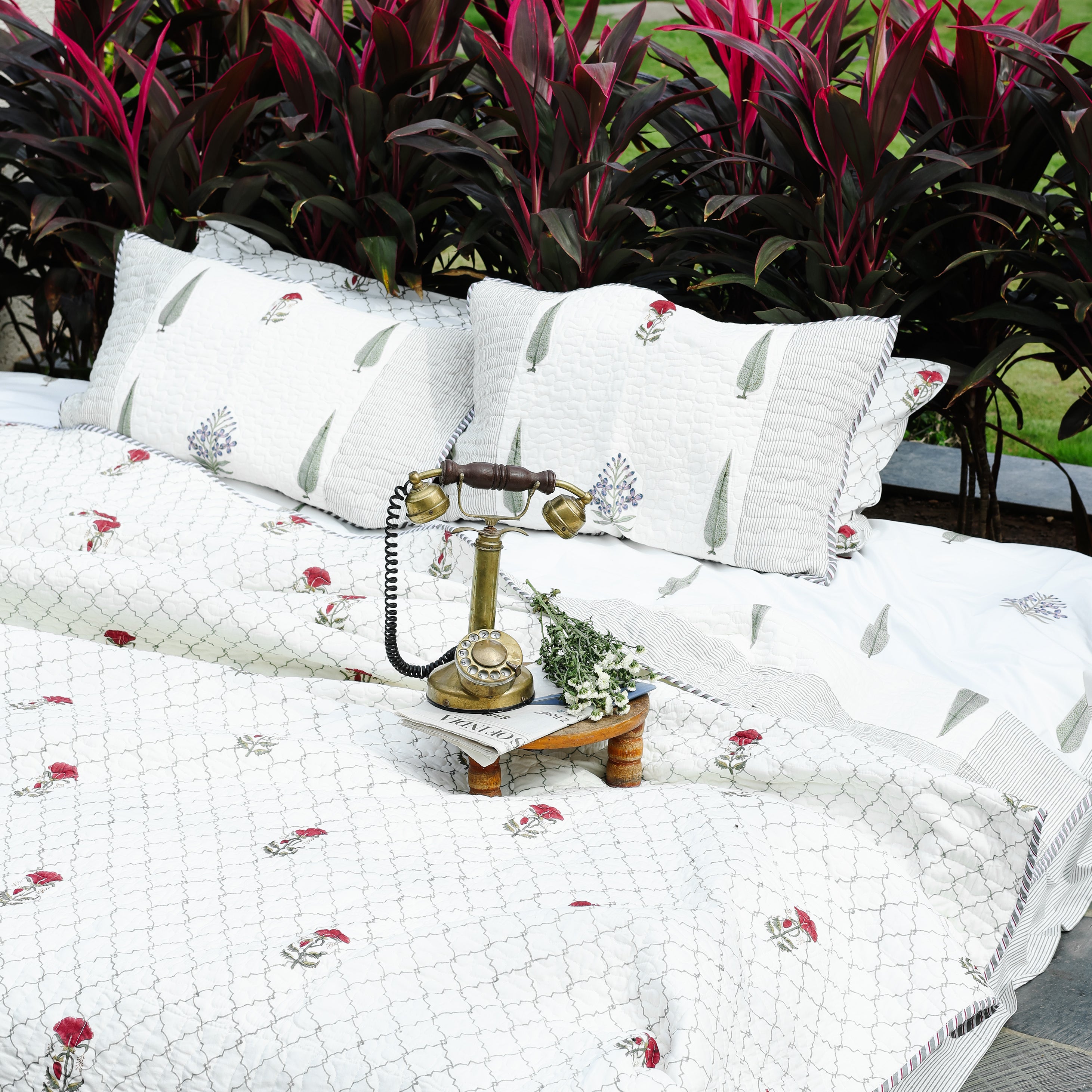 White cotton bedspread with floral hand block print on a bed in an outdoor setting with plants and a garden. Buy luxury bedspread. 