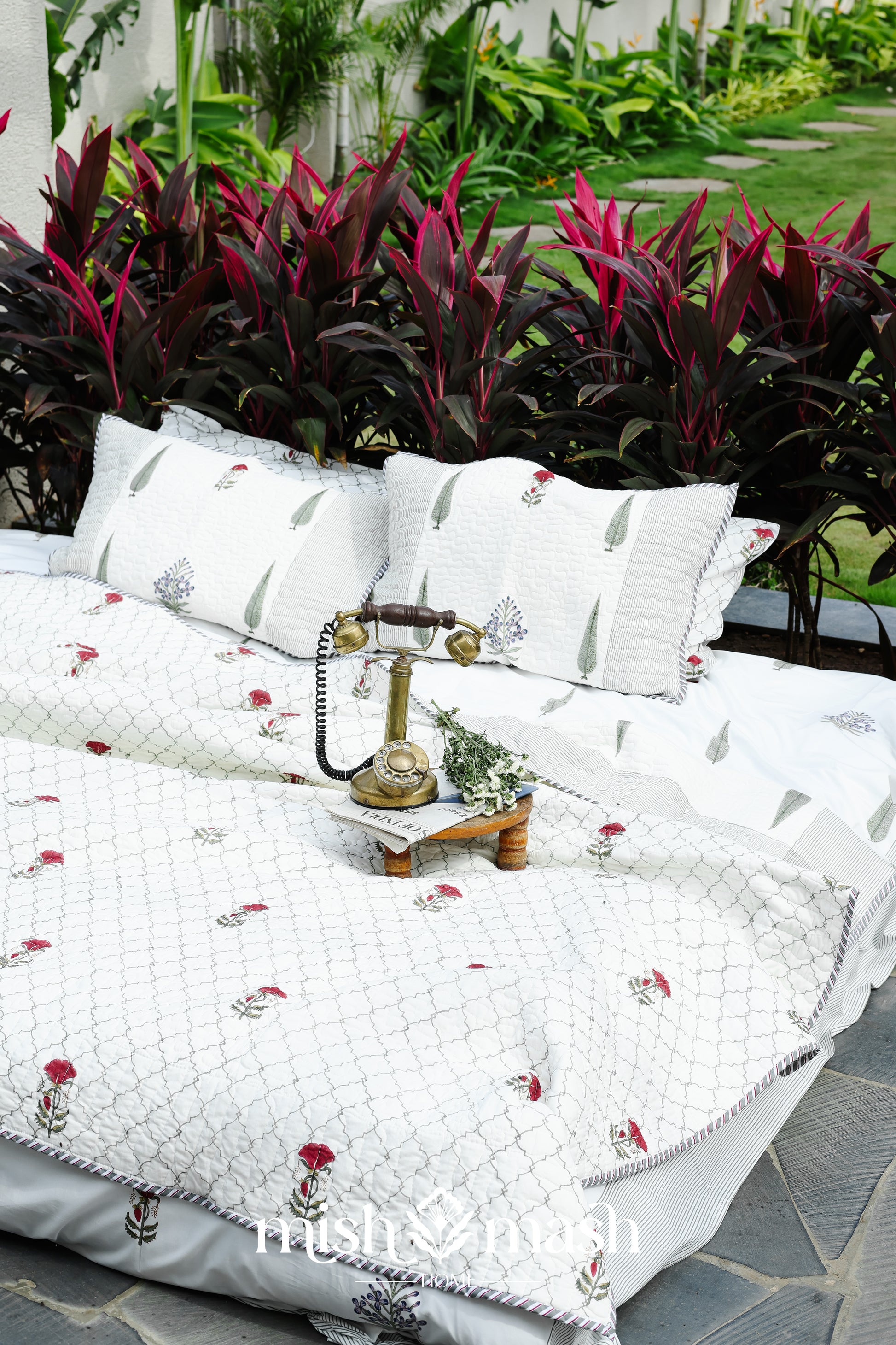 White cotton bedspread with floral hand block print on a bed in an outdoor setting with plants and a garden. Buy luxury bedspread. 