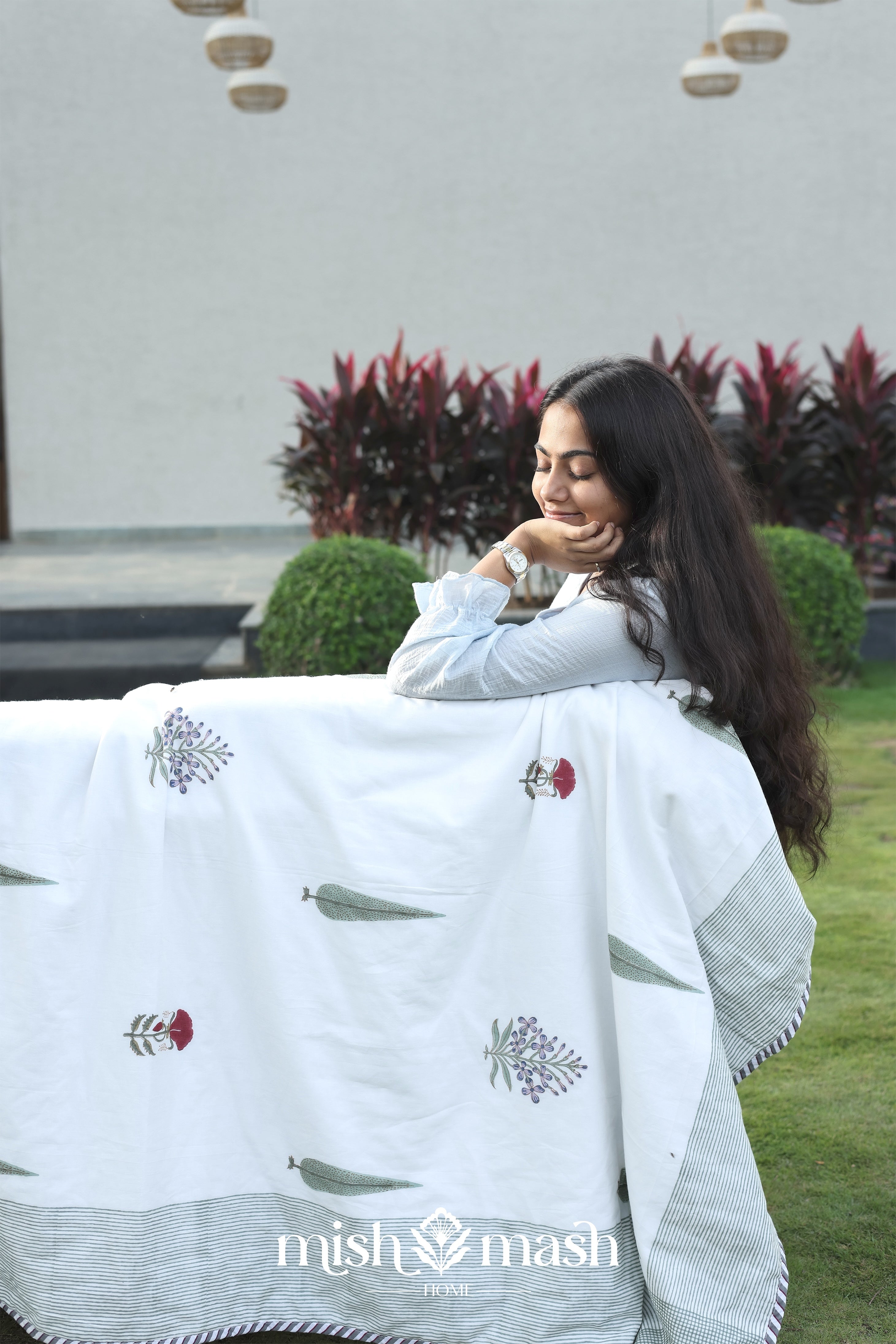 Woman wrapped in a white floral cotton dohar blanket with 'mish mash' branding in an outdoor setting. Cotton dohar.