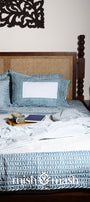Bed with blue and white geometric double bed bedsheet and a cotton bedspread and cotton dohar blanket on top.