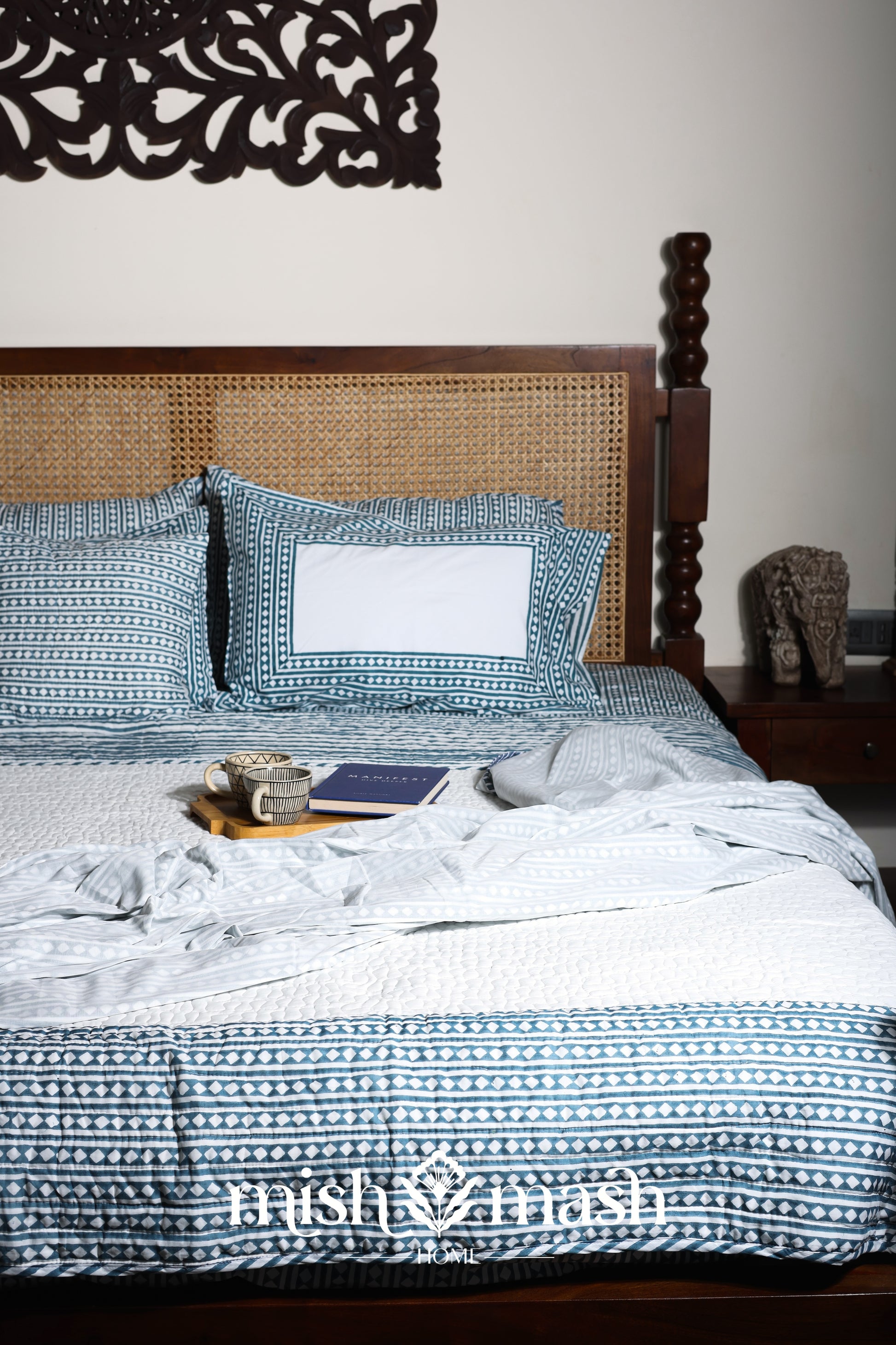 Bed with blue and white geometric double bed bedsheet and a cotton bedspread and cotton dohar blanket on top.