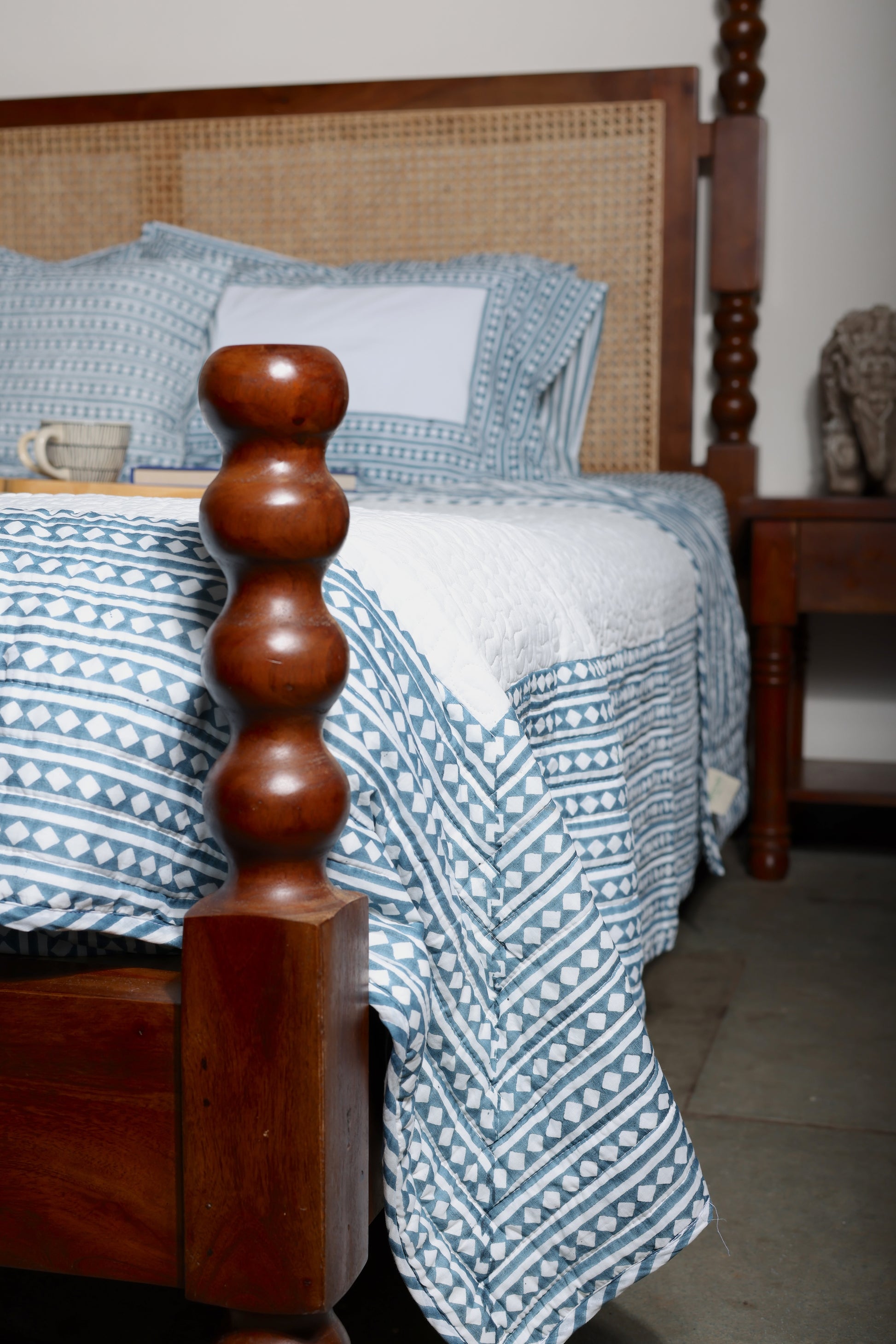 Bed with blue double bed bedsheet and quilted bed cover in a room setting. Buy pure cotton double bedsheet and luxury bedspread online.