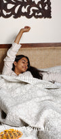 Woman lying in bed with a floral grey luxury bed spread 