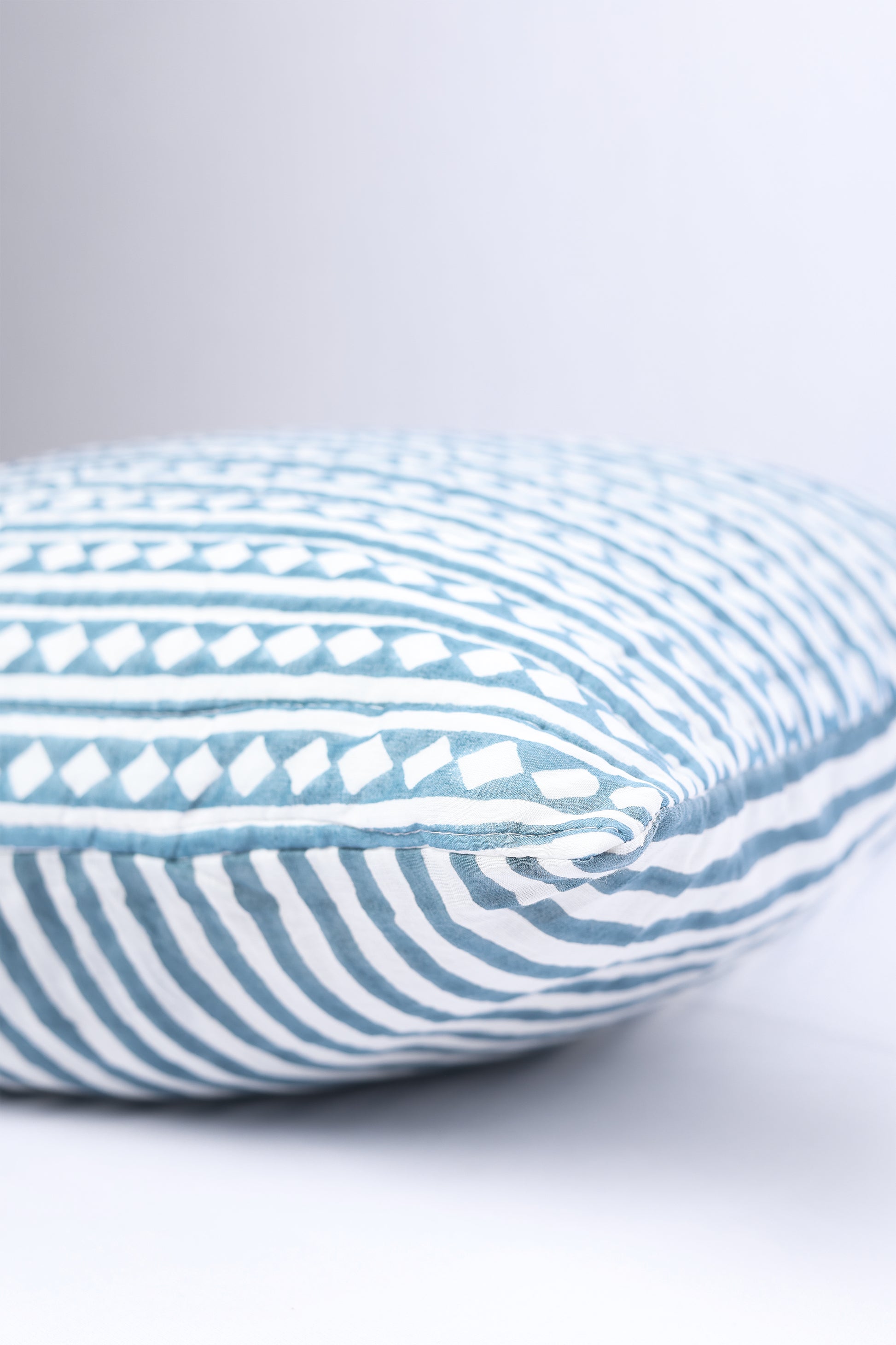 Cotton cushion cover with blue and white stripes on a light gray background. 