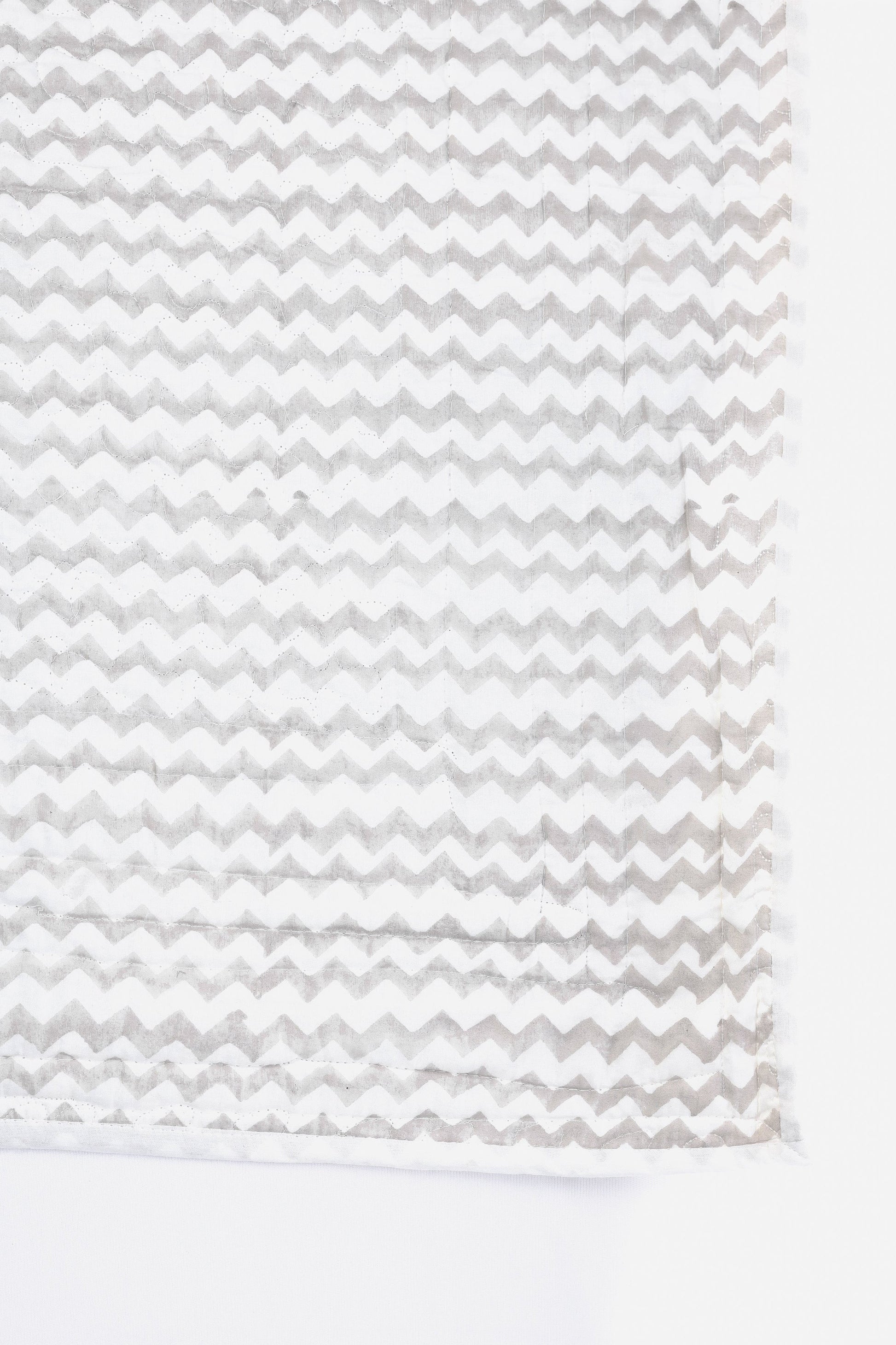 Quilted bed spread in cotton with grey chevron pattern on white background