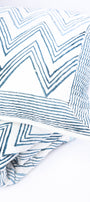 Blue and white zigzag patterned cotton  pillow kept on a matching blue reversible cotton bed spread