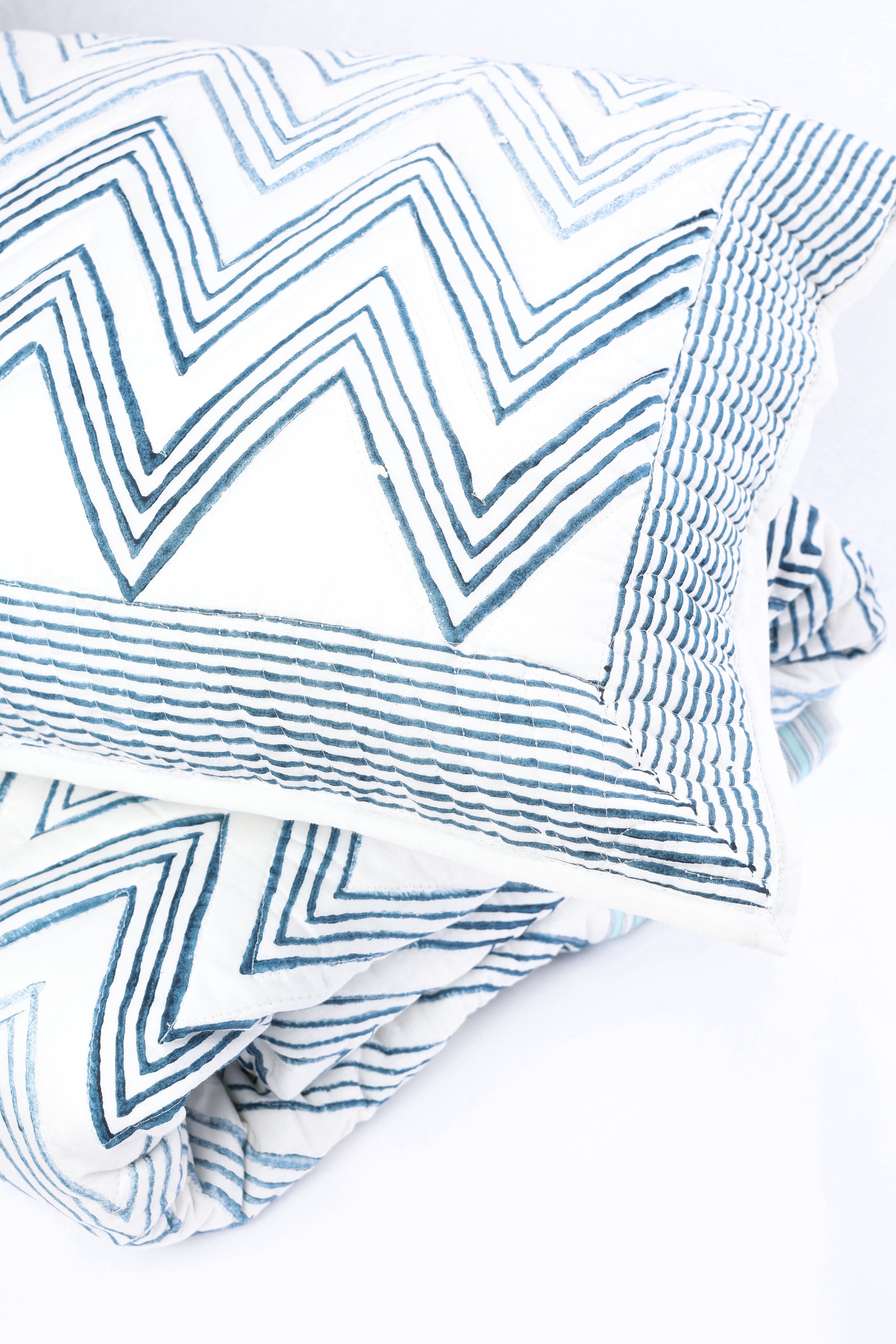Blue and white zigzag patterned cotton  pillow kept on a matching blue reversible cotton bed spread