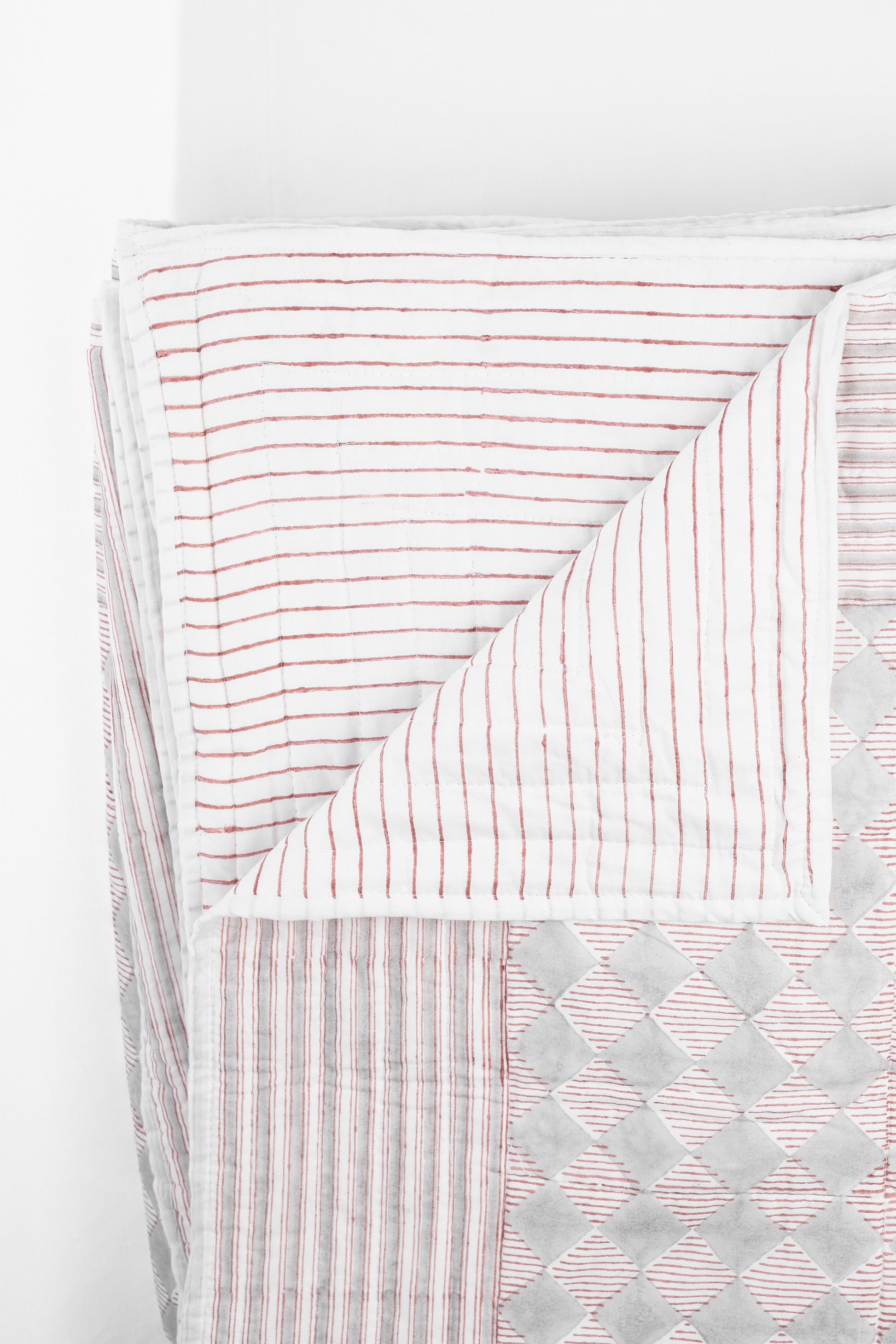 Red and white reversible quilted bed spread with grey checks on one side and red stripes on another side
