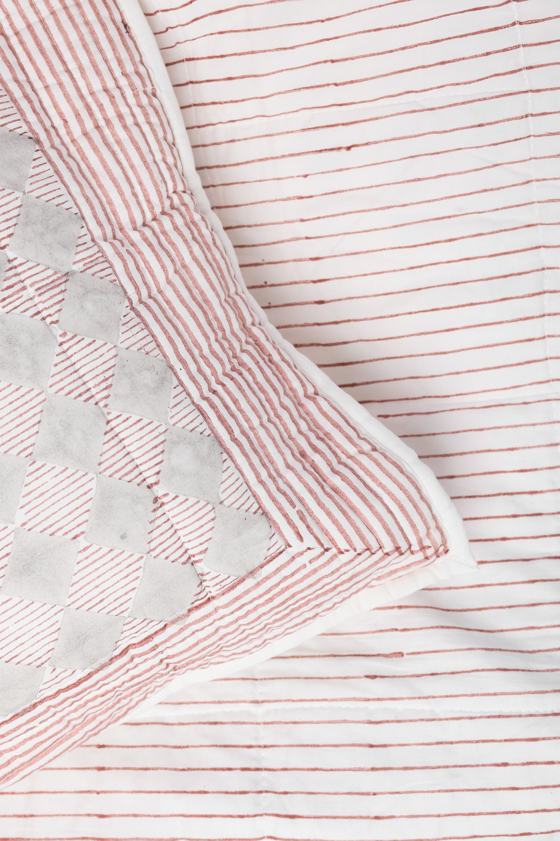 Close-up of a red and white striped quilted cotton bed spread with a  checkered pillow cover