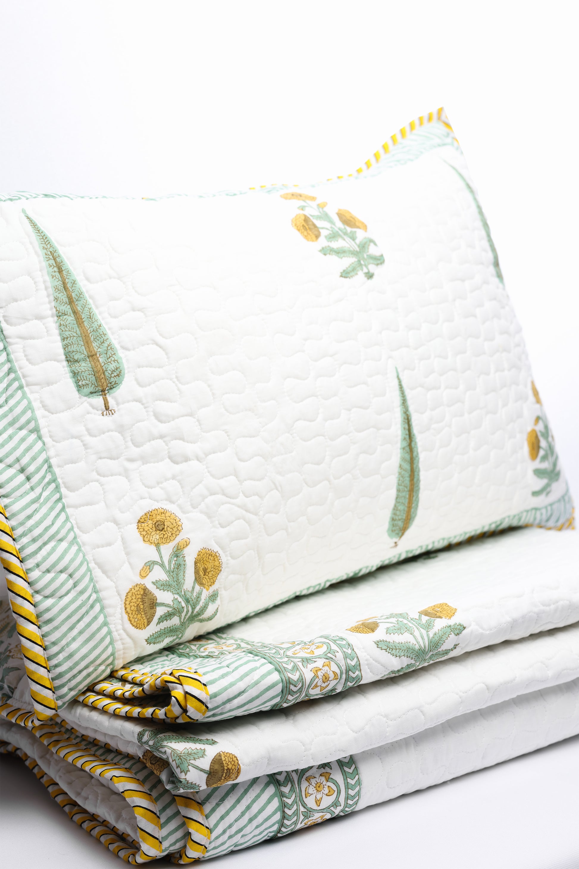Stack of floral double bed cover on a white background wih a matching white and yellow pillow cover.