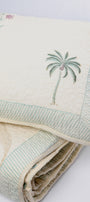 folded quilted cotton light yellow bed cover with palm tree motifs and a matching pillow cover