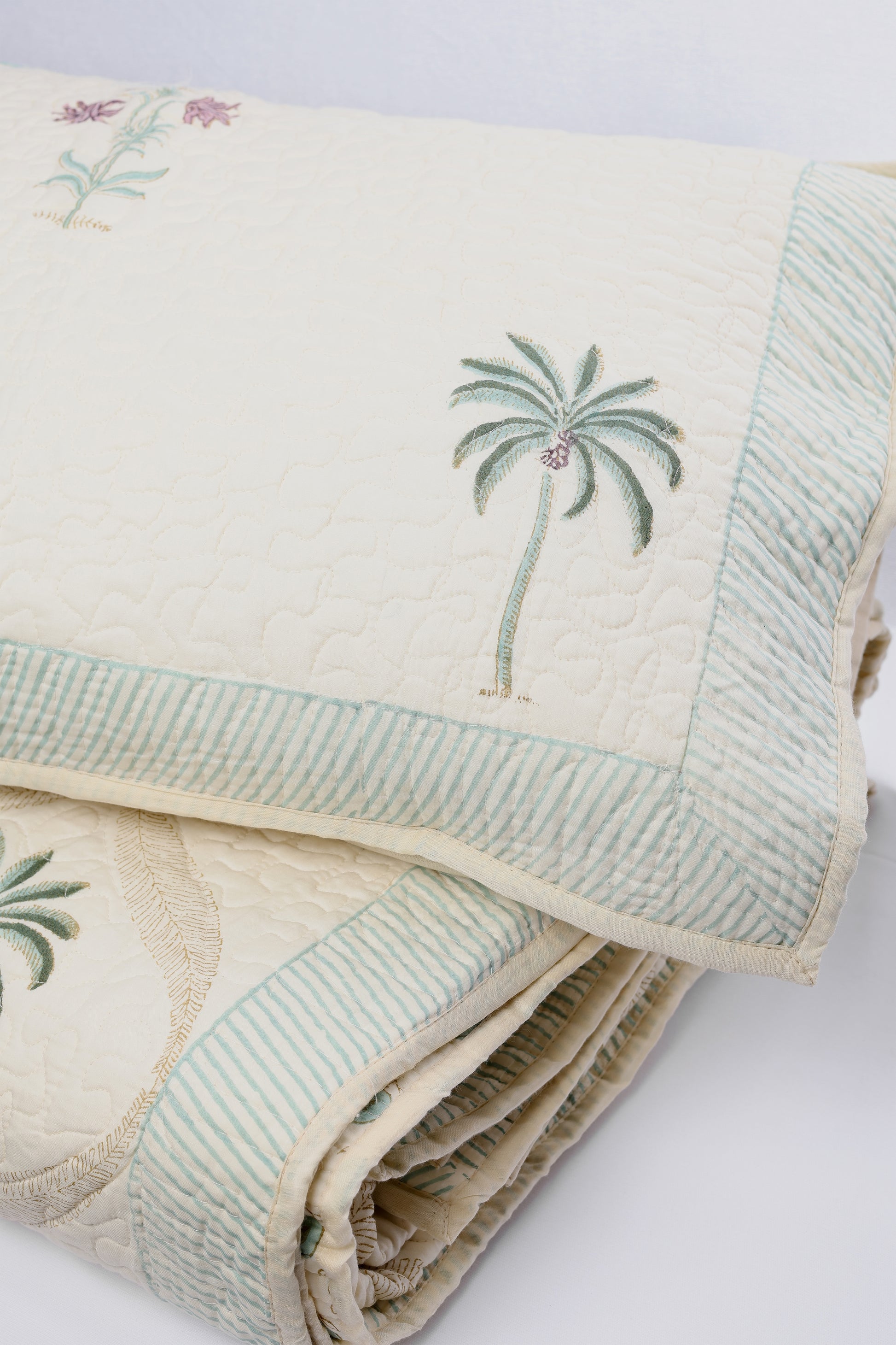 folded quilted cotton light yellow bed cover with palm tree motifs and a matching pillow cover