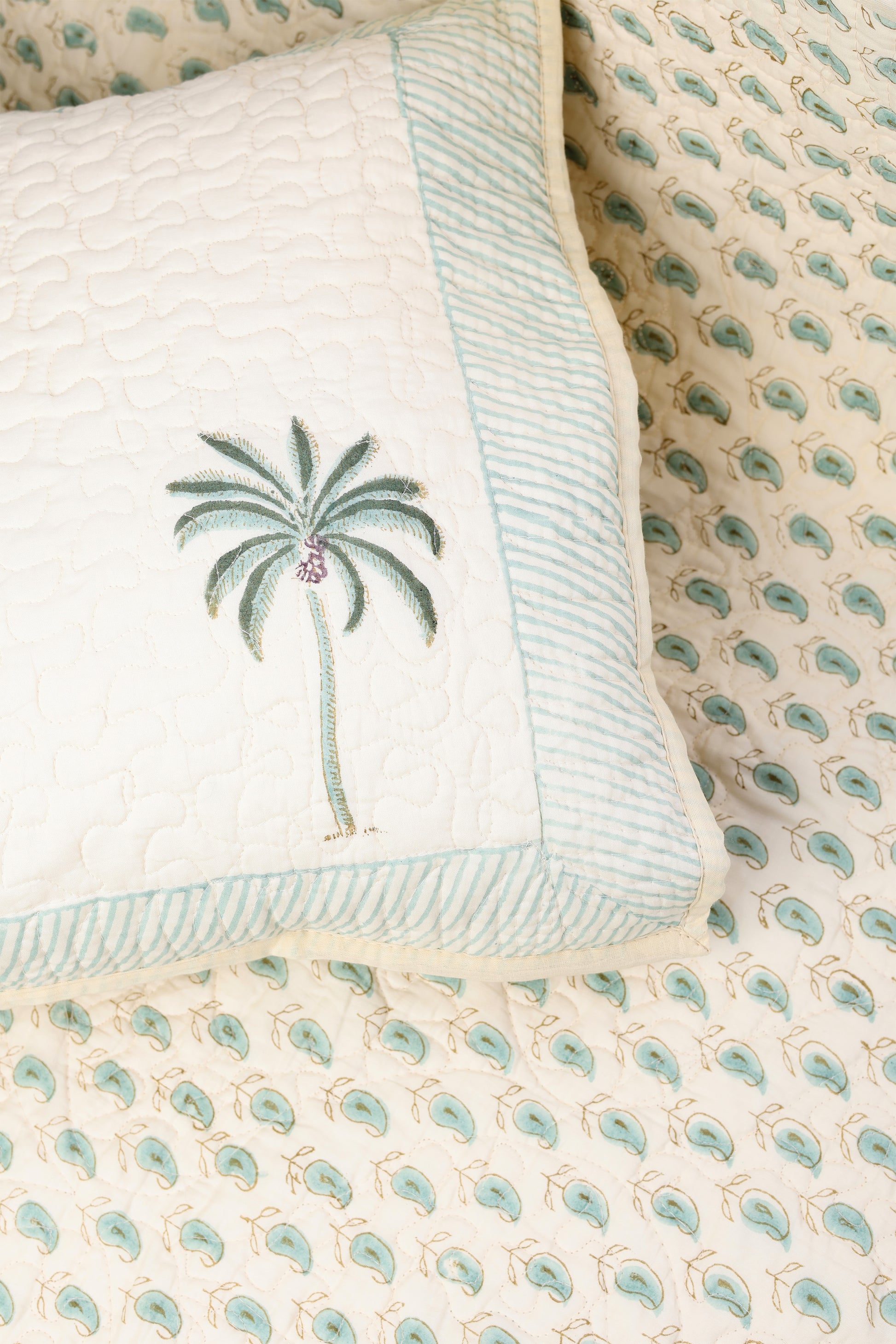 Close-up of a quilted luxury bed spread with paisley design and a matching cotton pillow with palm tree design in light yellow. Luxury bed spread online.