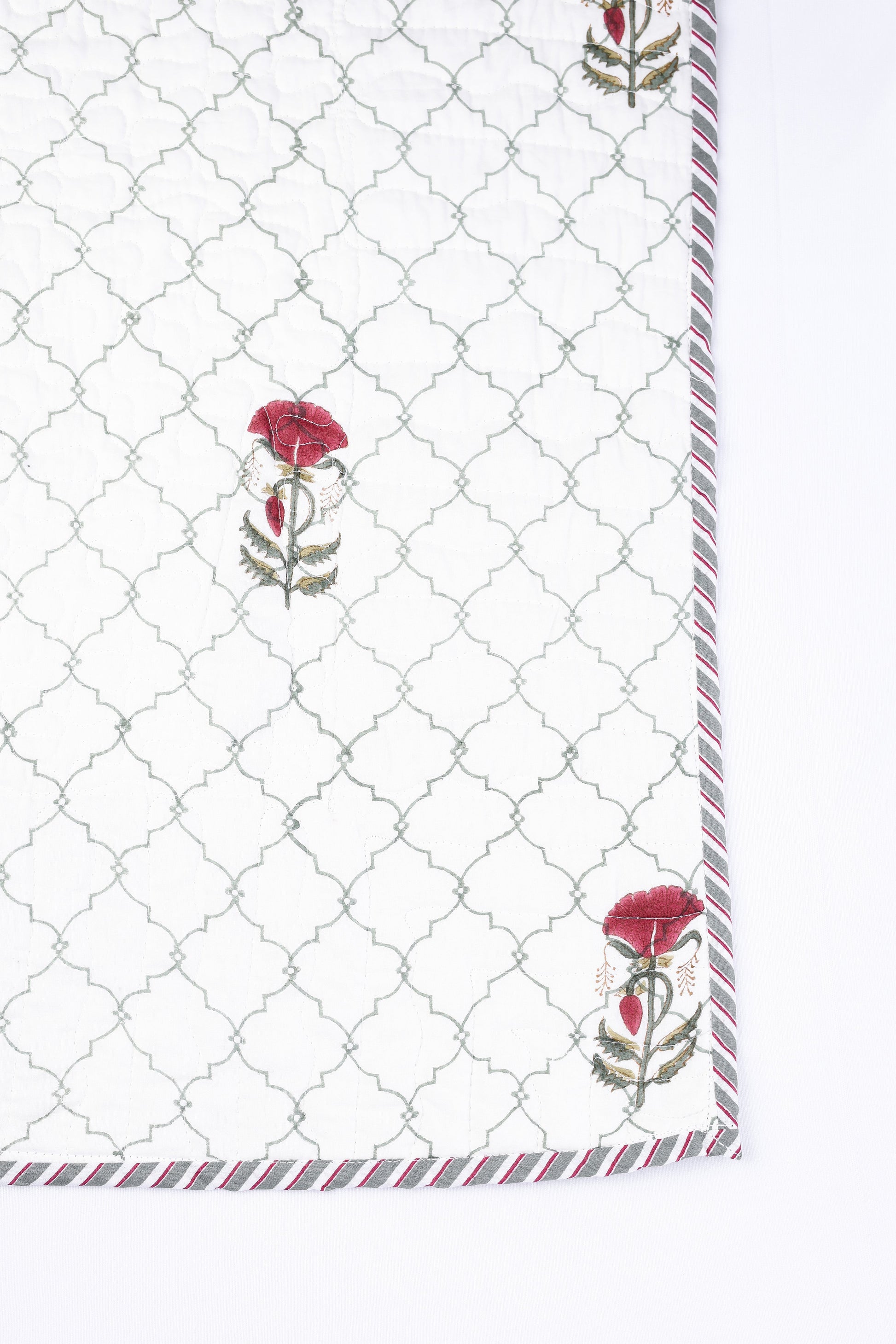 Quilted cotton bed cover with a geometric pattern and floral hand block print on a white background. Festive bedcover.